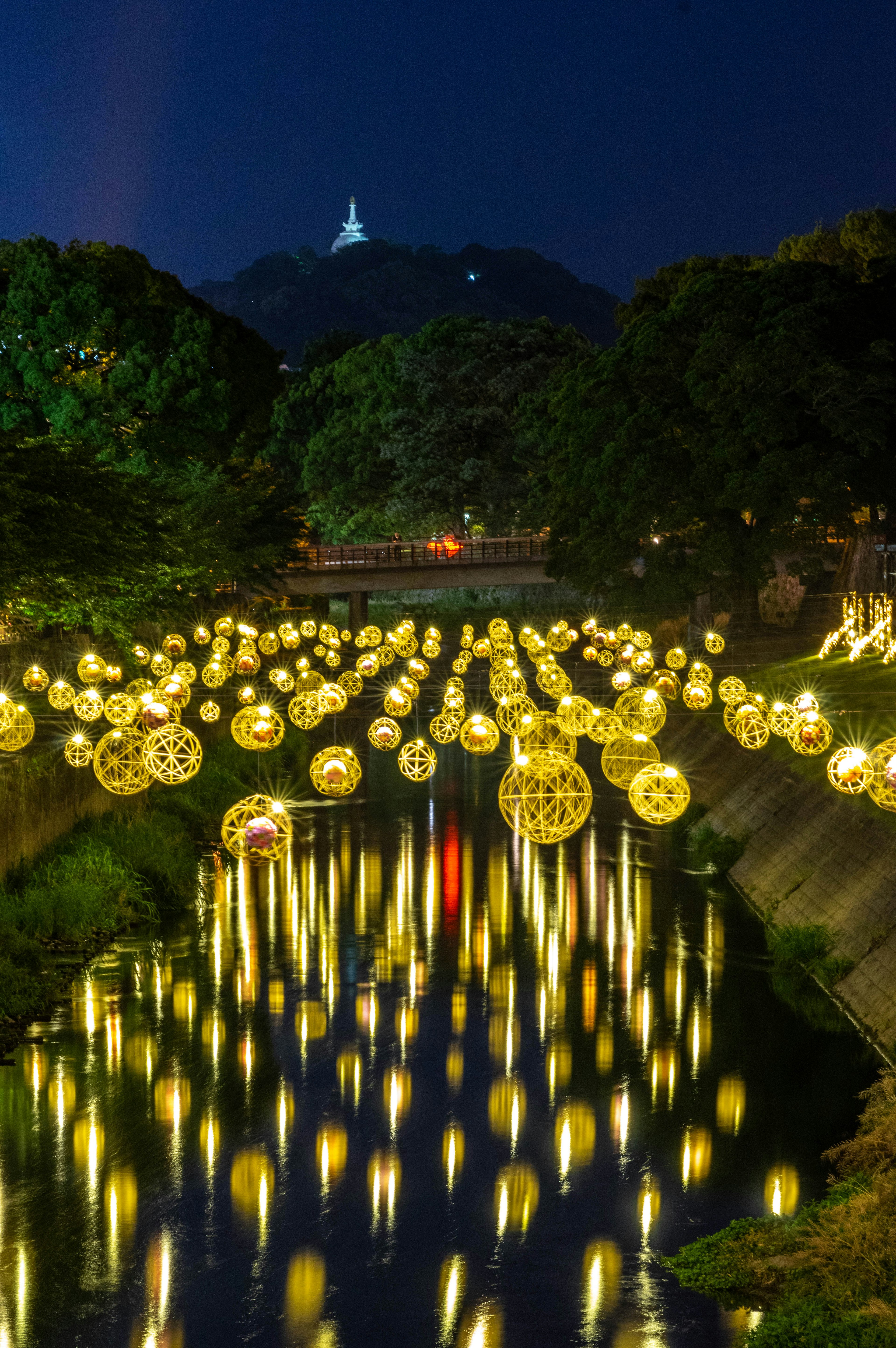 Lampion mengapung memantulkan cahaya di sungai pada malam hari dengan pemandangan gunung di kejauhan