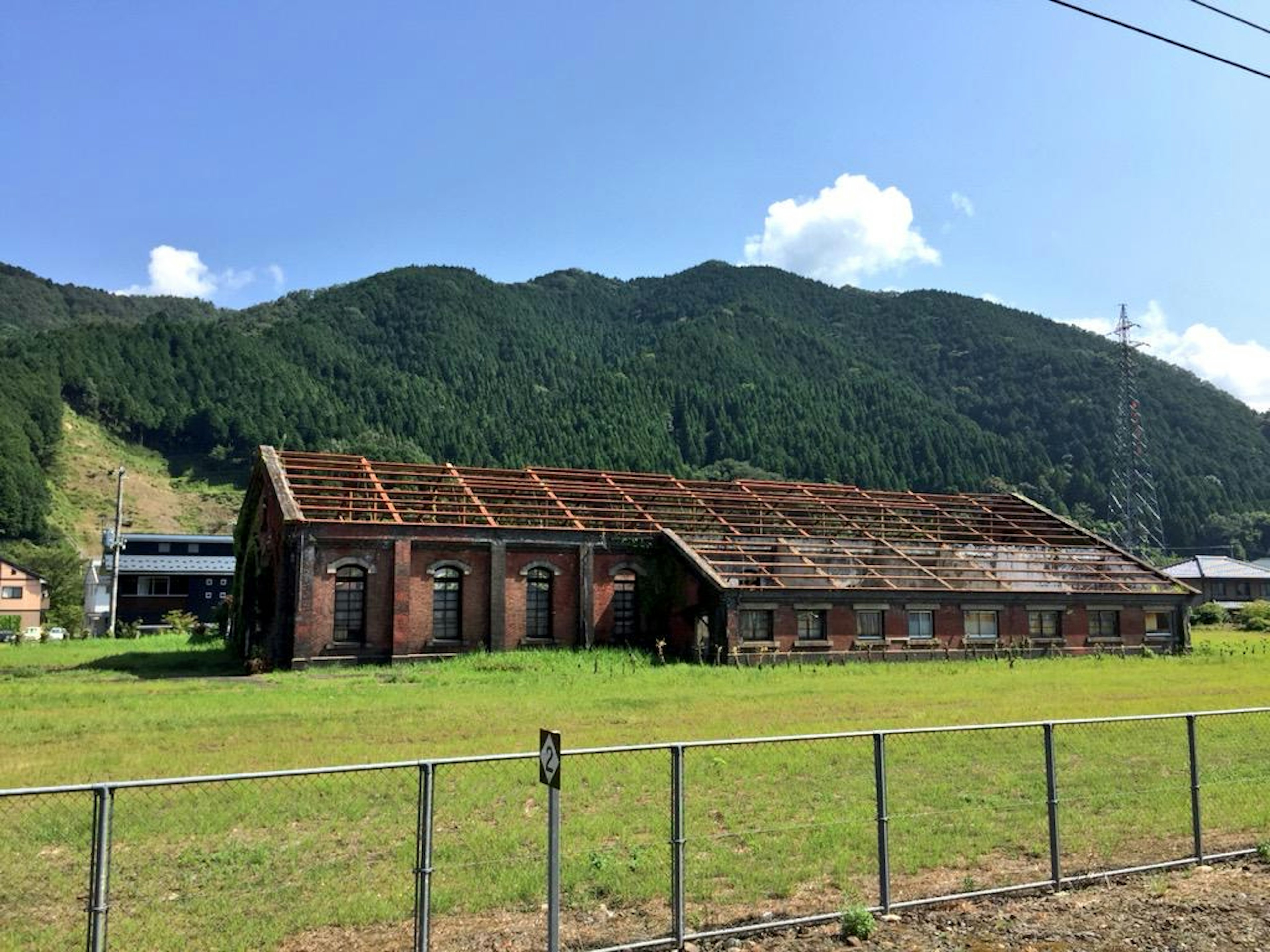 Old brick building surrounded by grass, damaged roof, mountains in the background