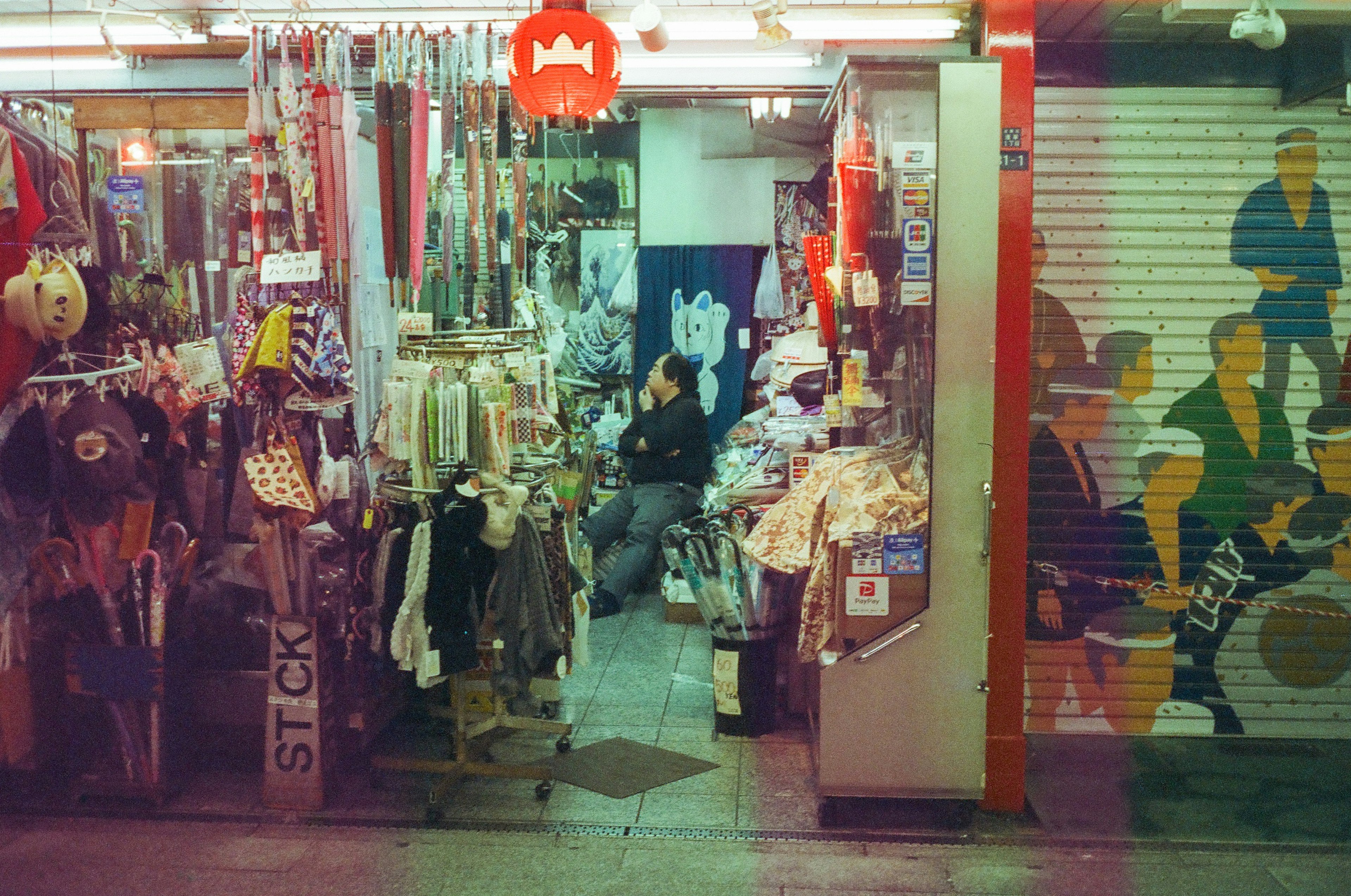 Entrada de un animado mercado callejero con tiendas que exhiben ropa y accesorios una persona sentada al fondo