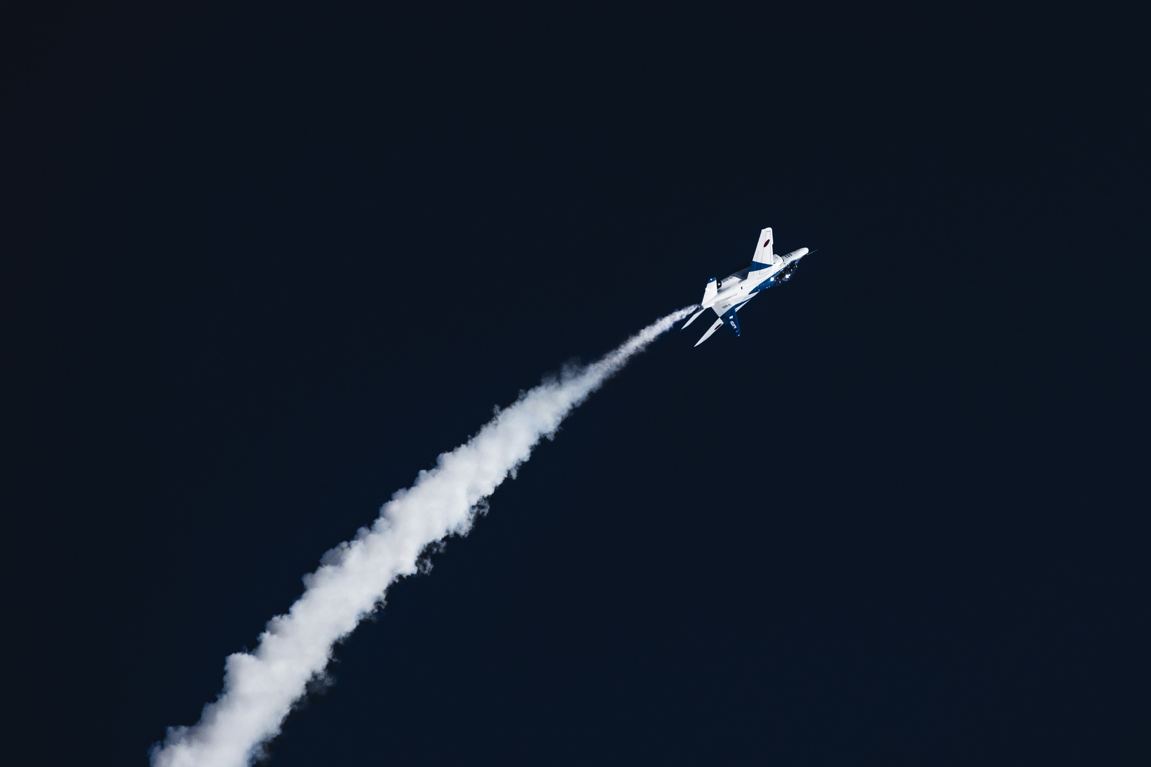 Ein weißes Flugzeug steigt mit einer Rauchspur gegen einen blauen Himmel auf