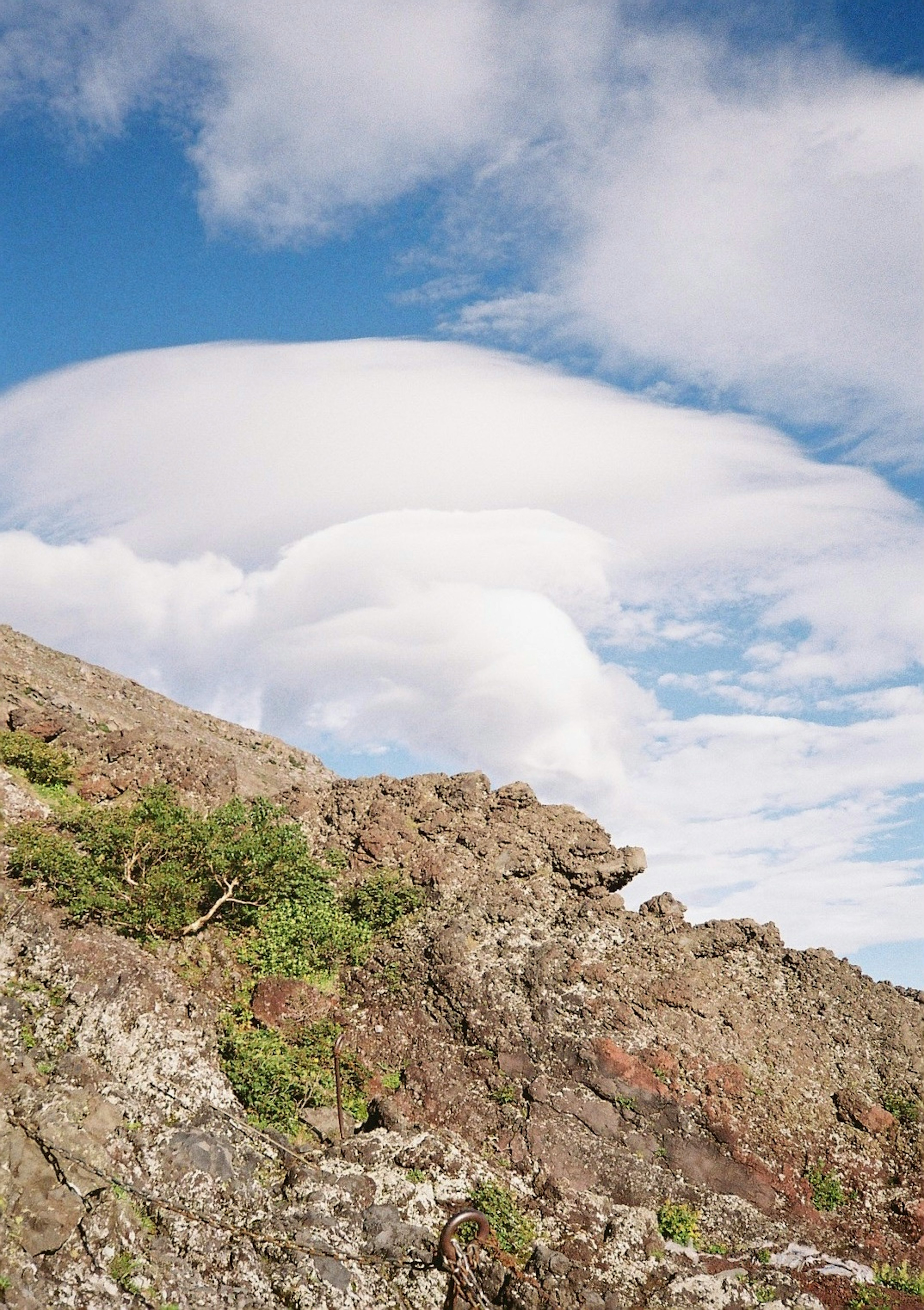 Nuvole lenticolari sopra un terreno roccioso con cielo blu