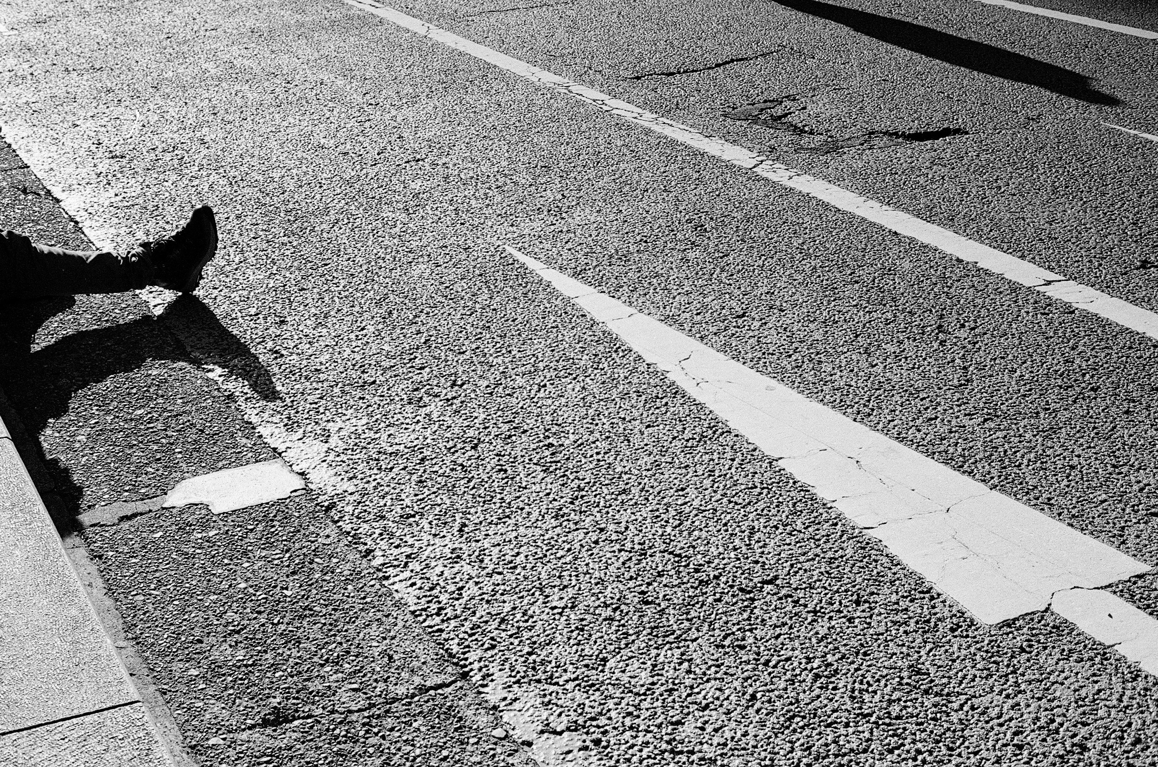 Black and white image showing a person's leg resting beside a road