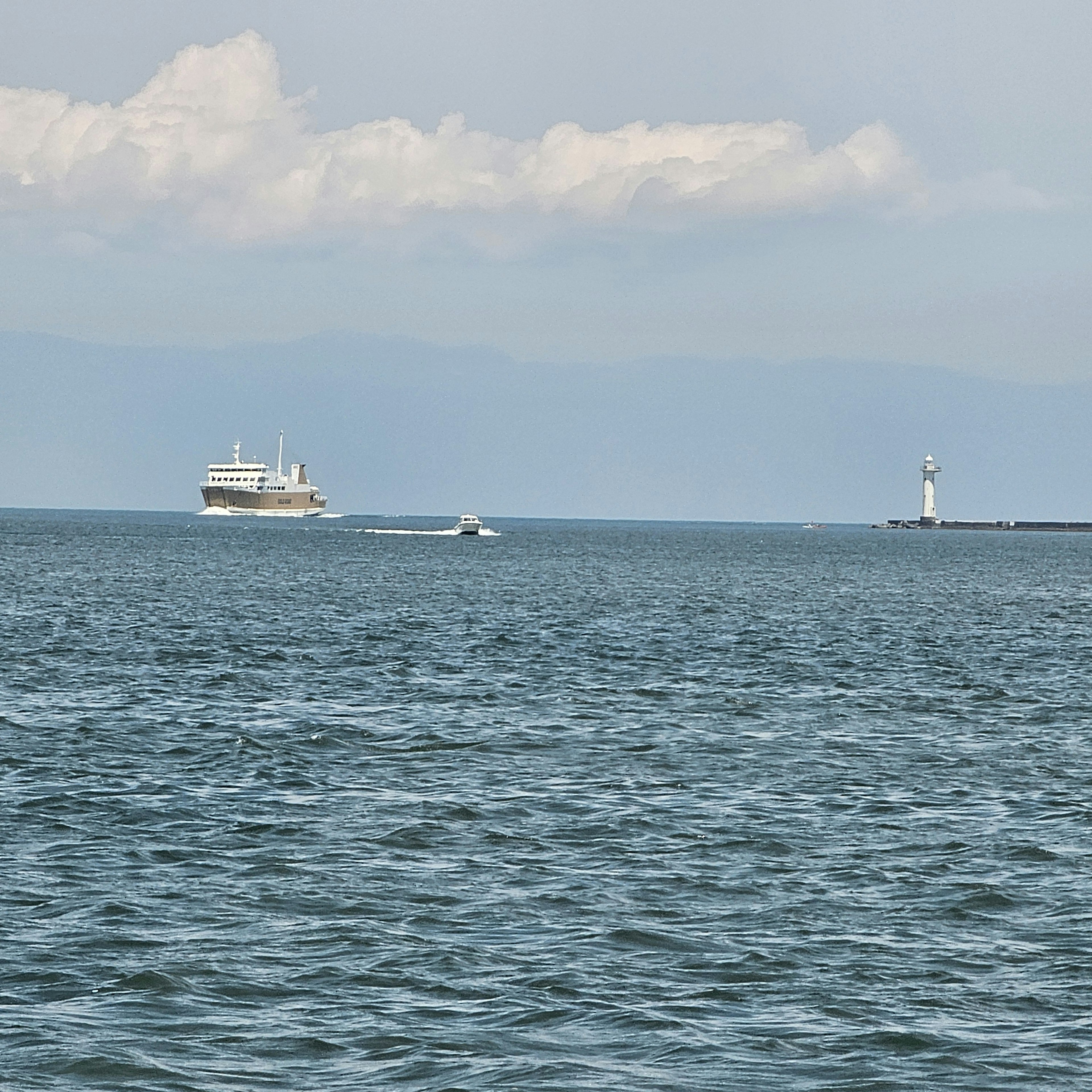 A view of a ship on the water with a lighthouse in the distance