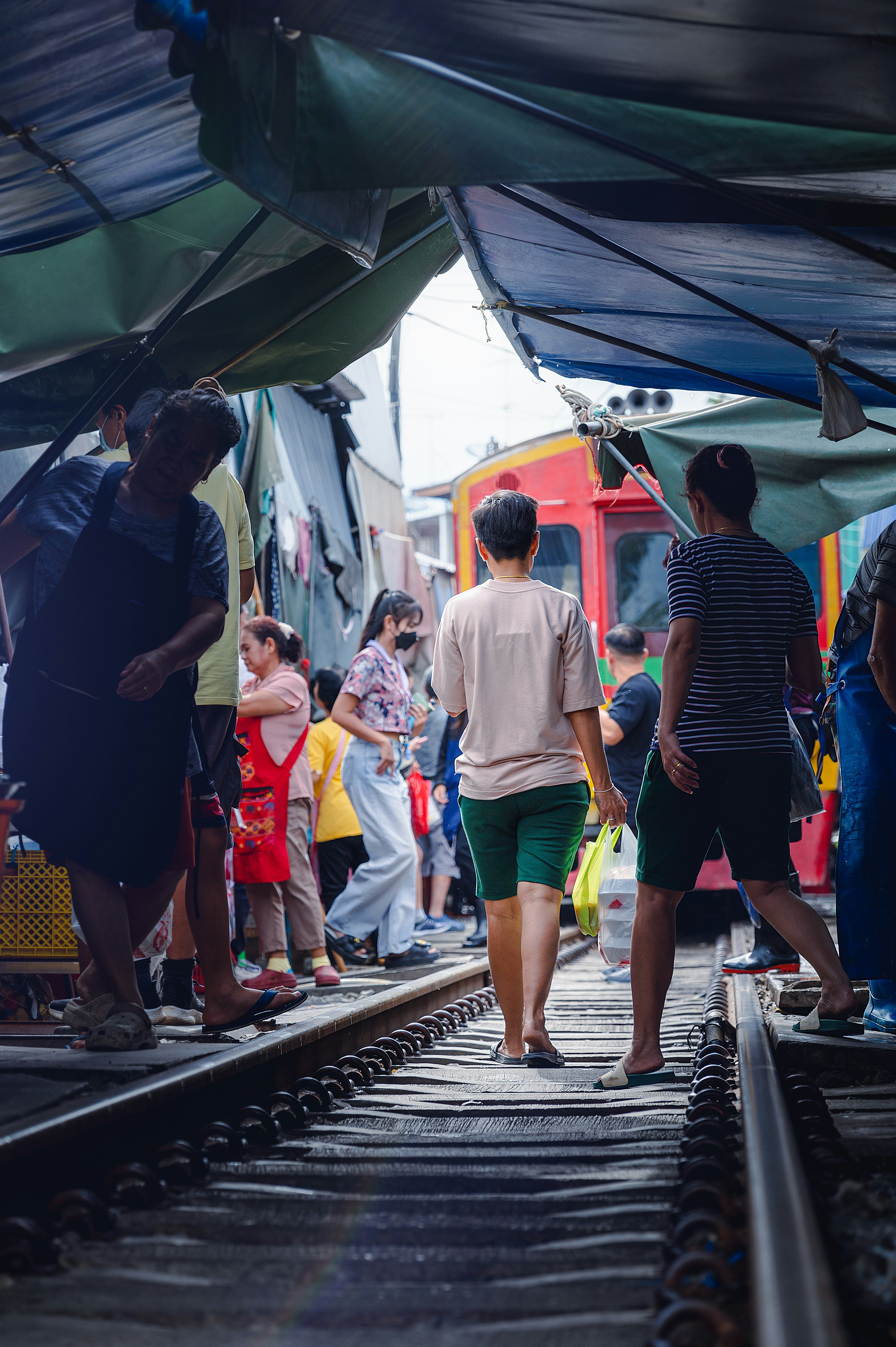 ผู้คนเดินอยู่บนรางรถไฟมีแผงขายของอยู่ด้านบน