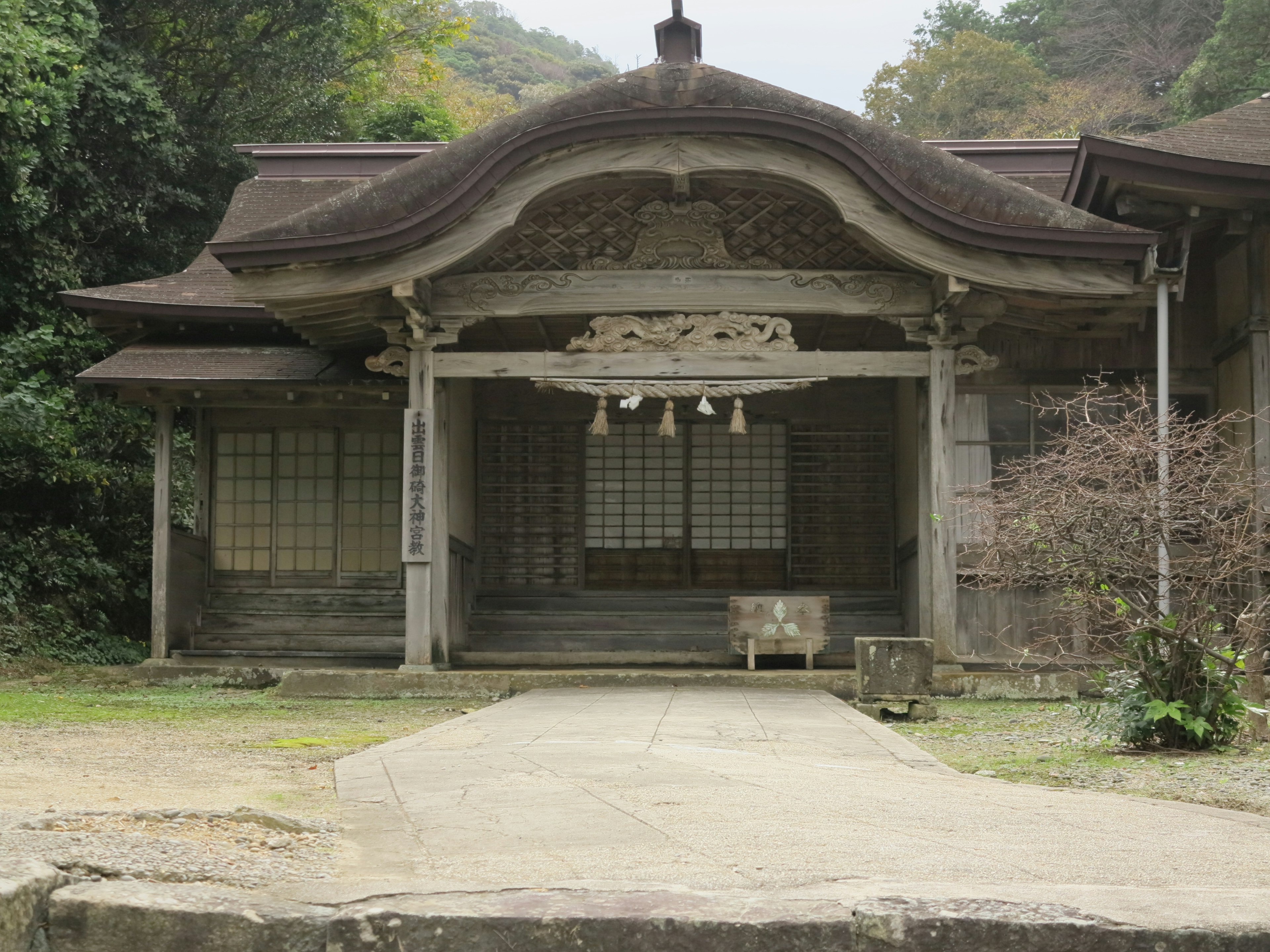 古い神社建築の外観 前庭に石の台座と木製の屋根