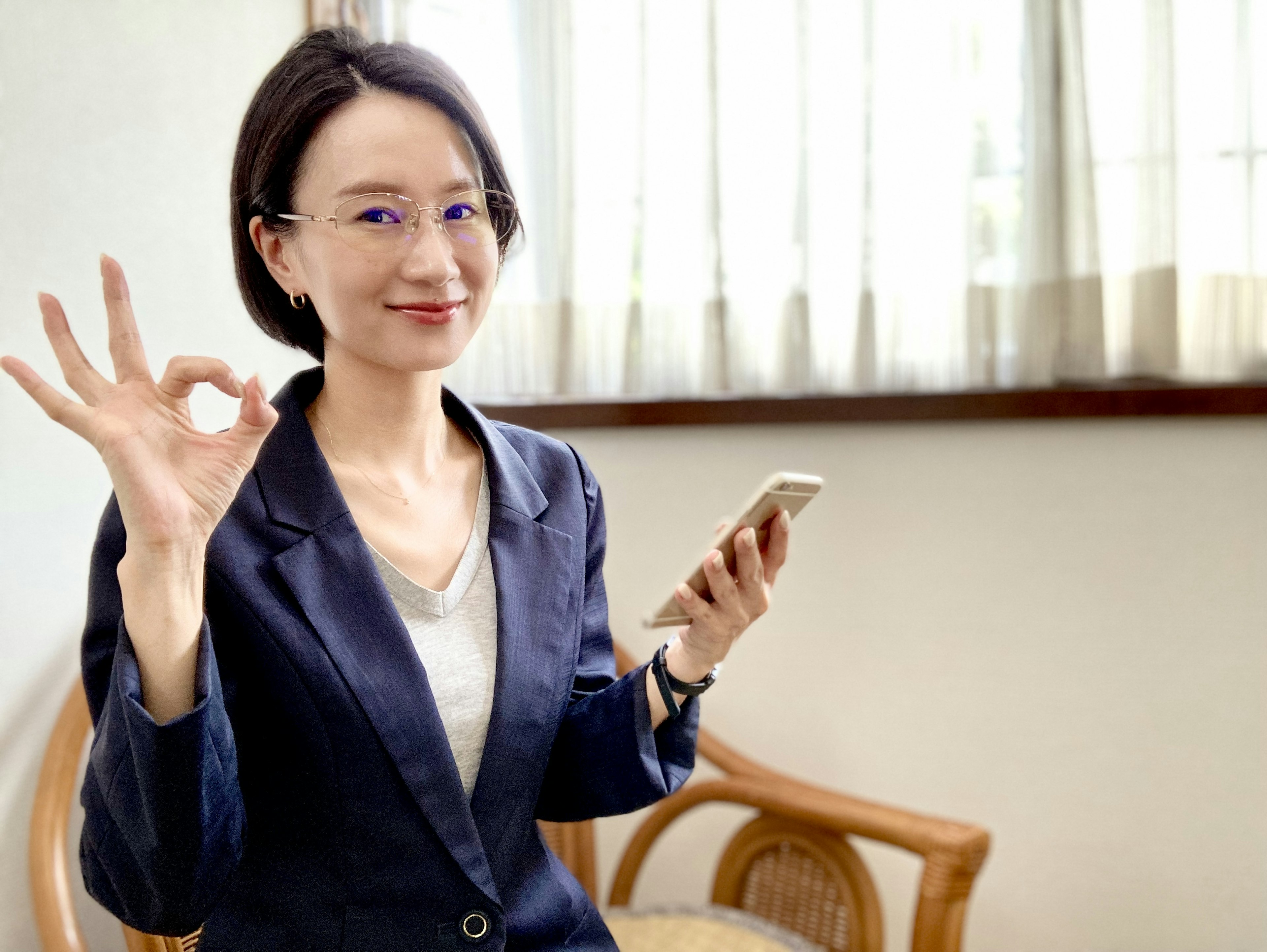 A woman in a smart business suit holding a smartphone making an OK gesture