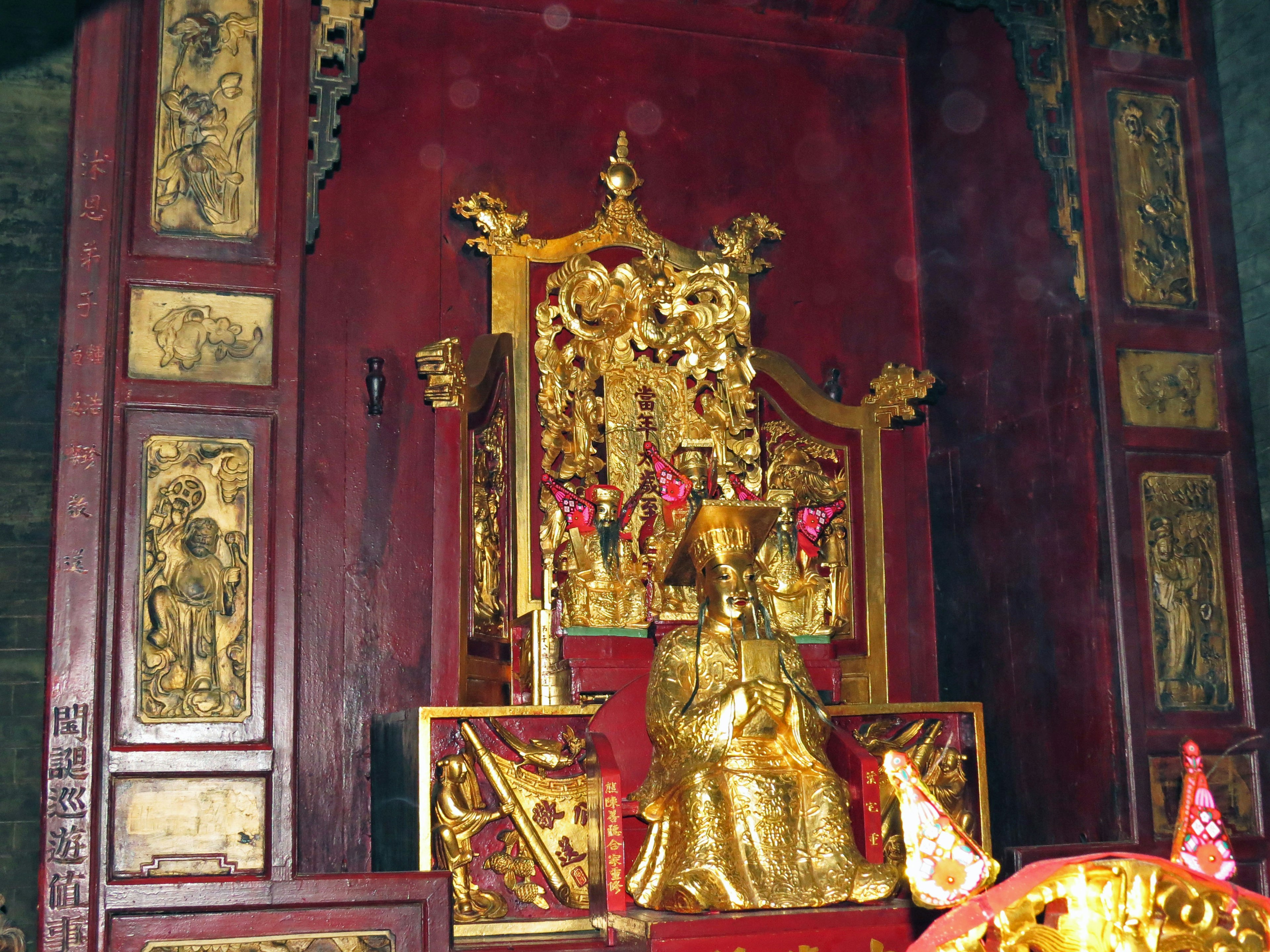 Golden Buddha statue seated on a red altar with intricate carvings