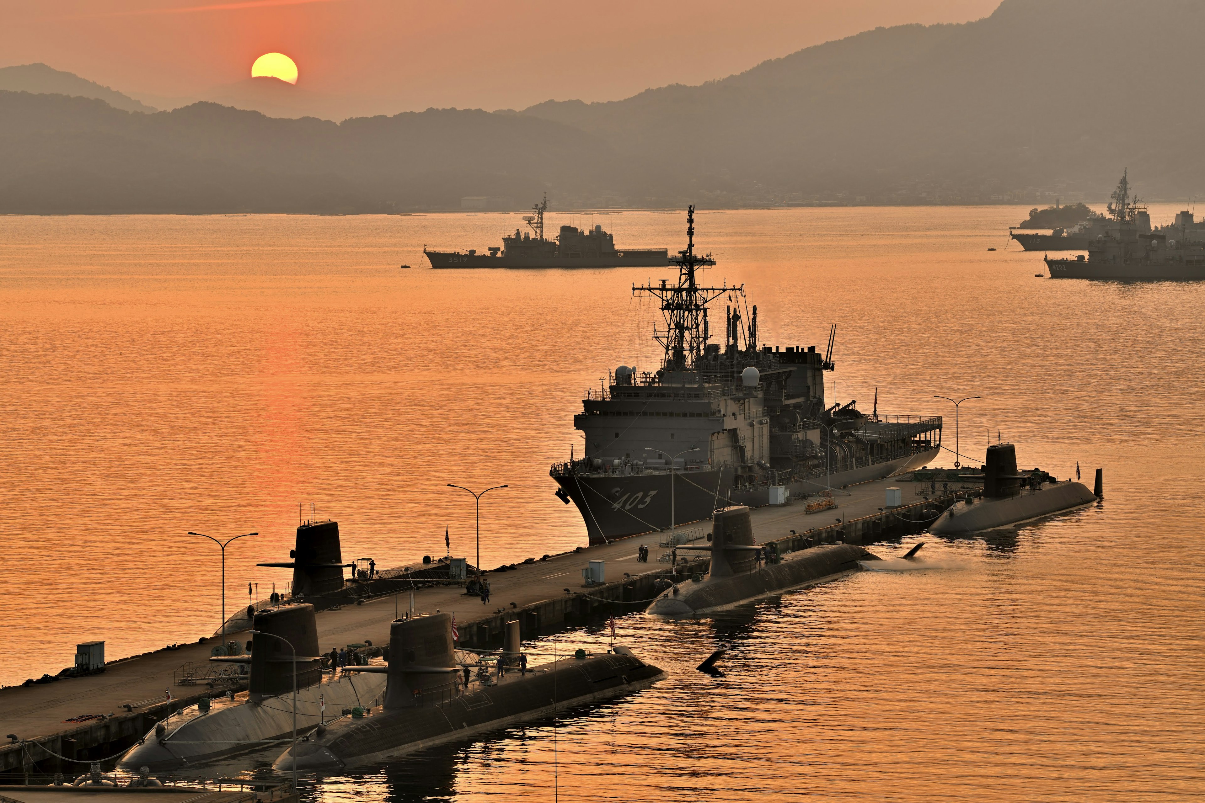 A naval ship docked at a pier during sunset over calm waters