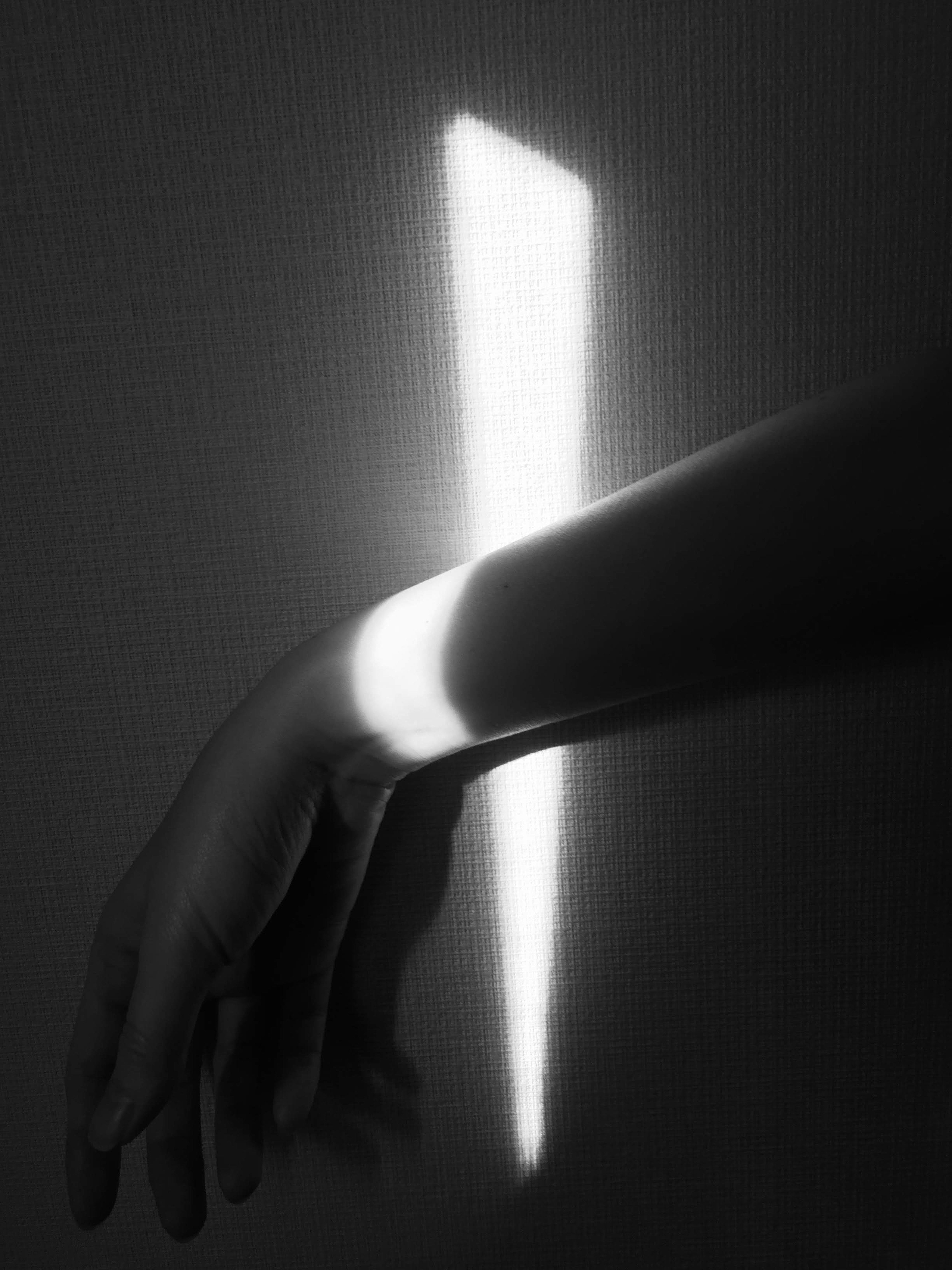 Immagine in bianco e nero di una mano con un fascio di luce sul polso