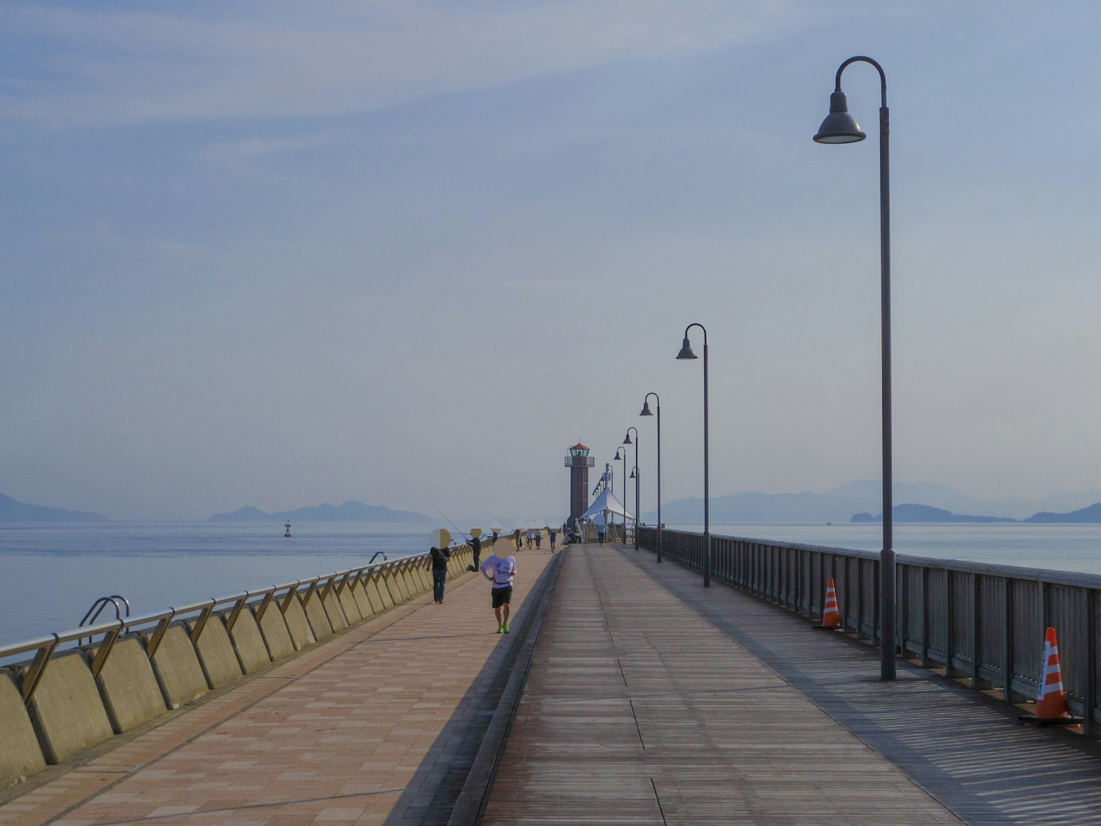 Des gens se promenant sur une jetée en bord de mer avec des lampadaires et des montagnes au loin