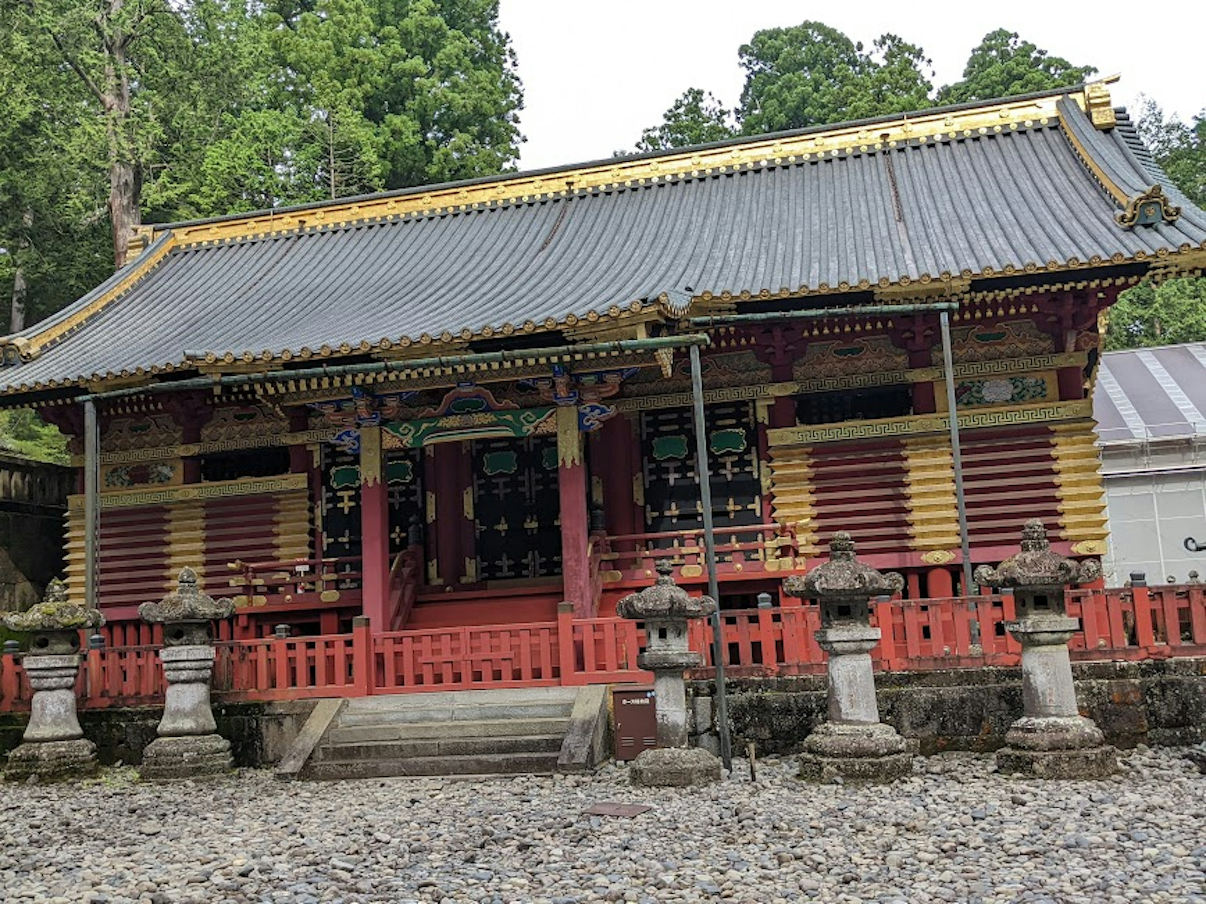 Bâtiment de temple traditionnel avec des piliers et un toit rouges entouré de lanternes en pierre