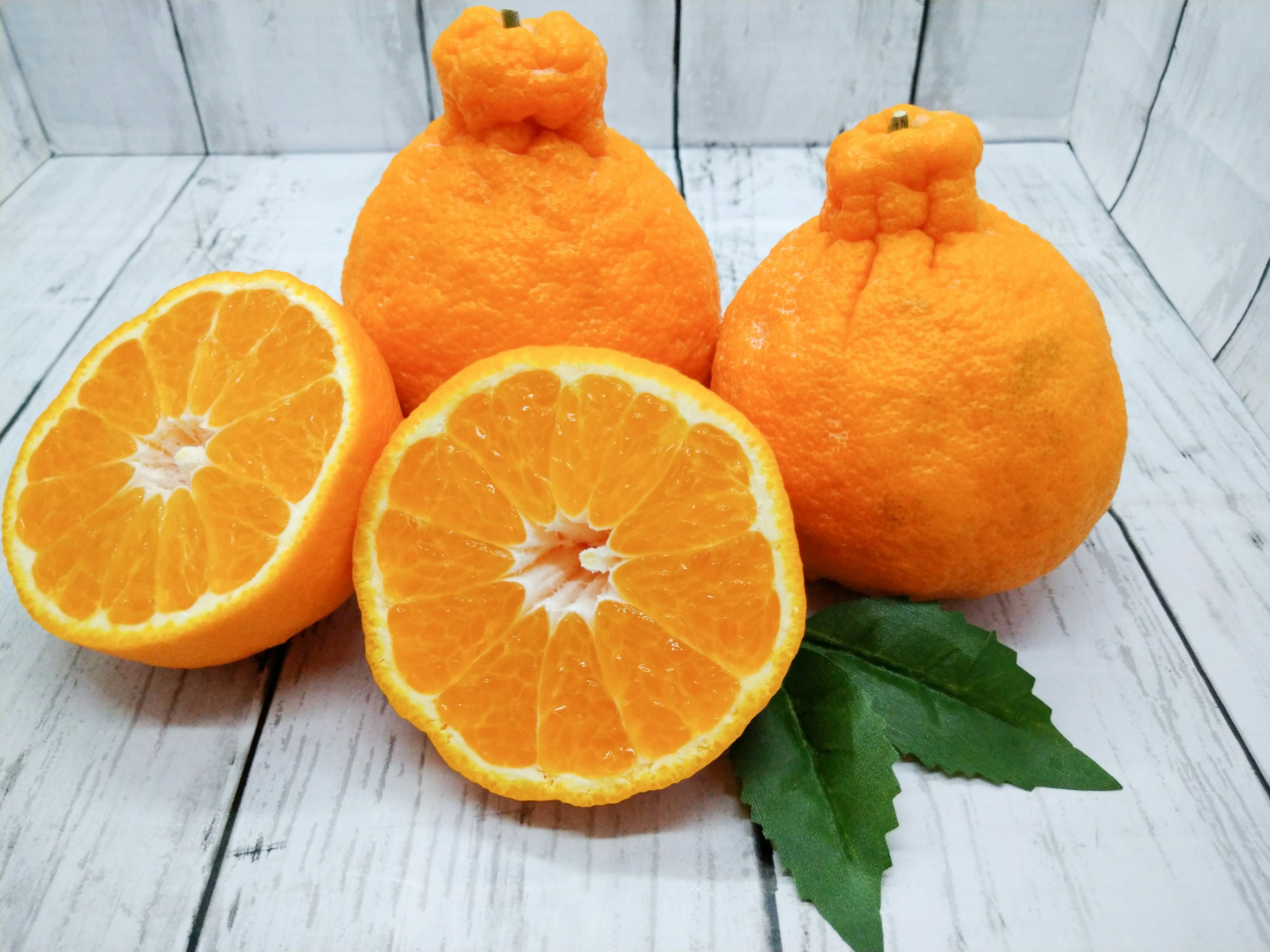 Three oranges with one sliced in half showing the bright orange flesh and green leaves