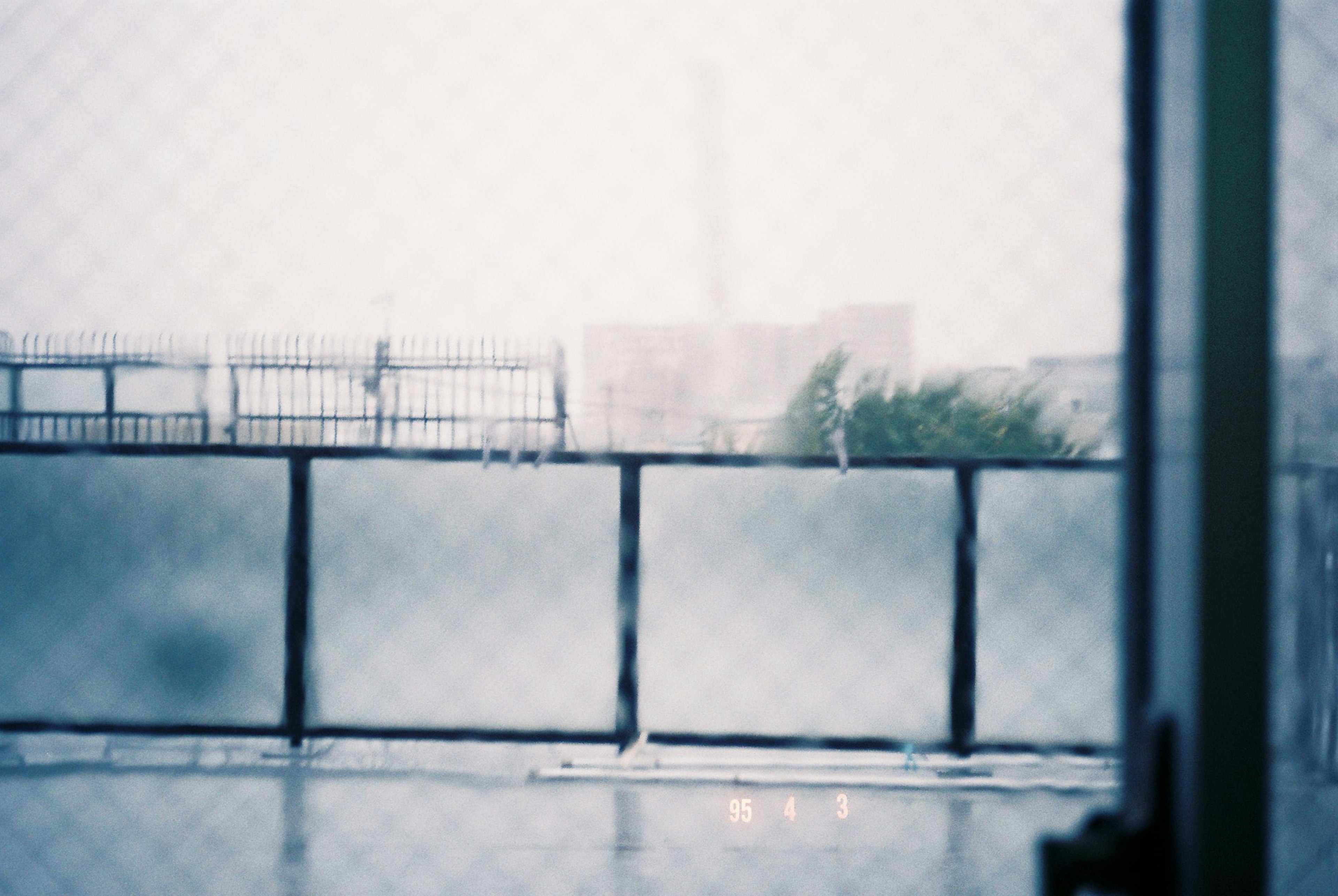 雨に濡れた窓越しに見えるぼんやりした風景とフェンス