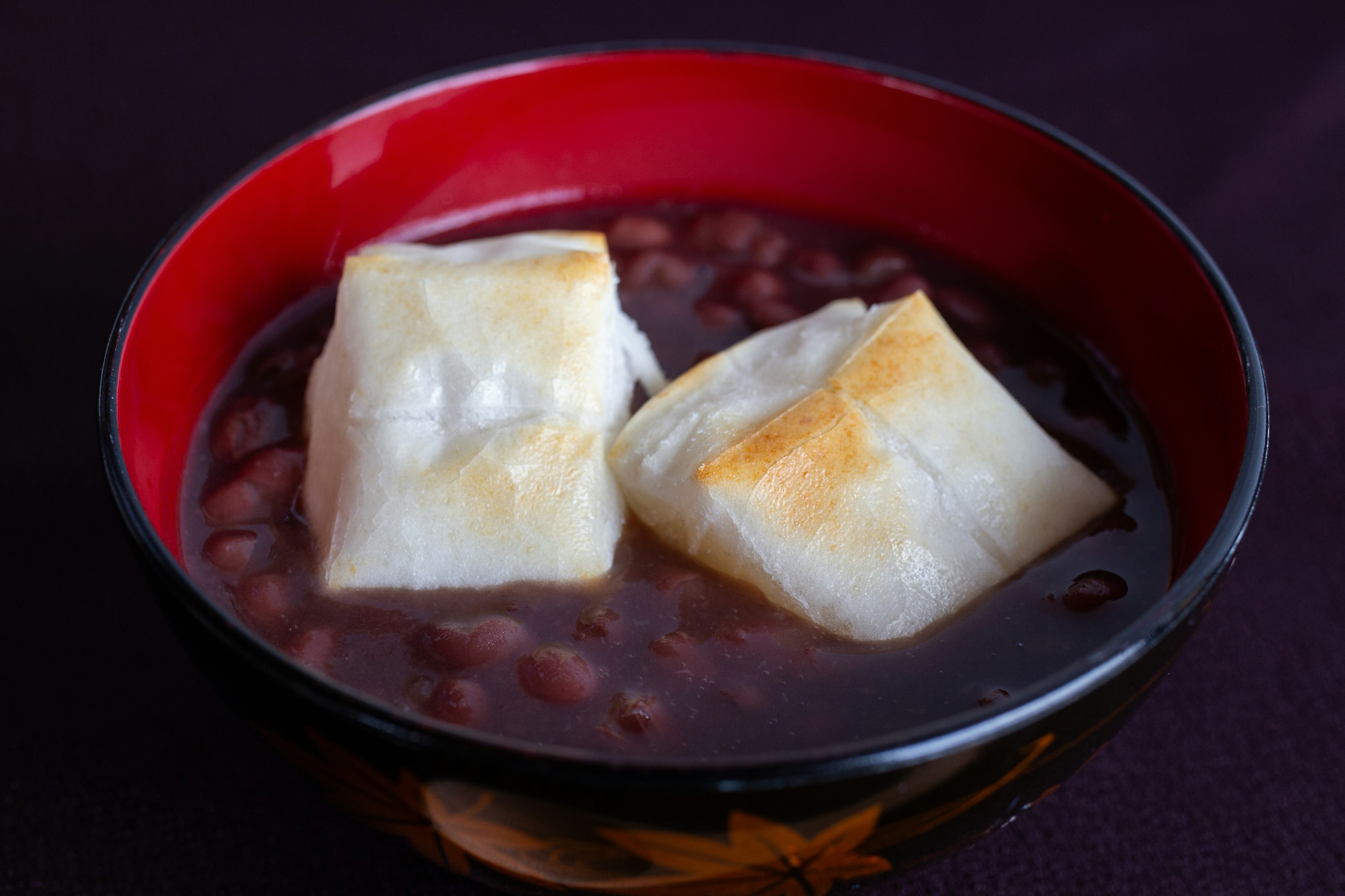 Süße rote-Bohnen-Suppe mit gerösteten Reiskuchen in einer roten Schüssel