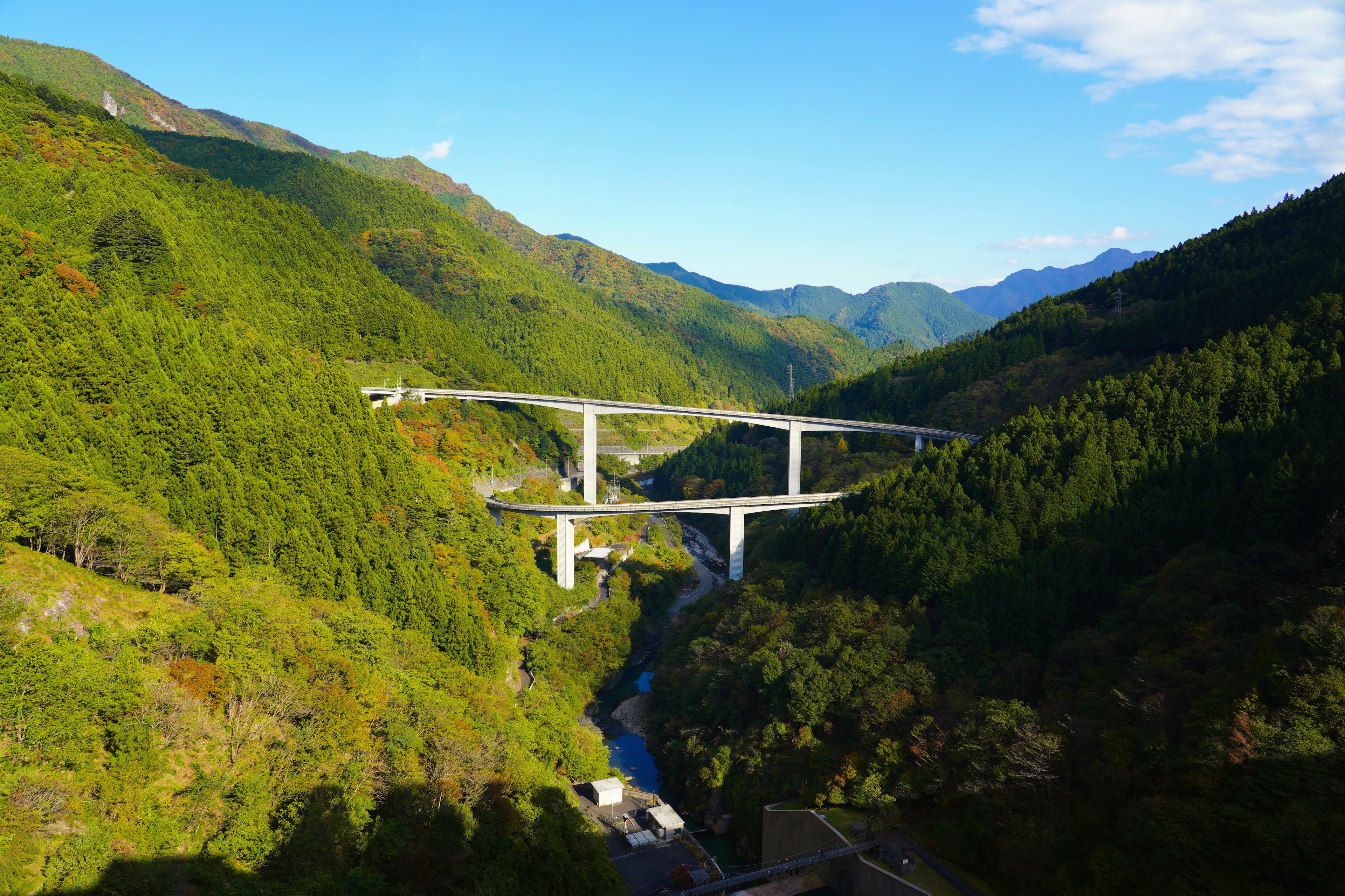 Sebuah jembatan tinggi melintasi pegunungan hijau di bawah langit biru