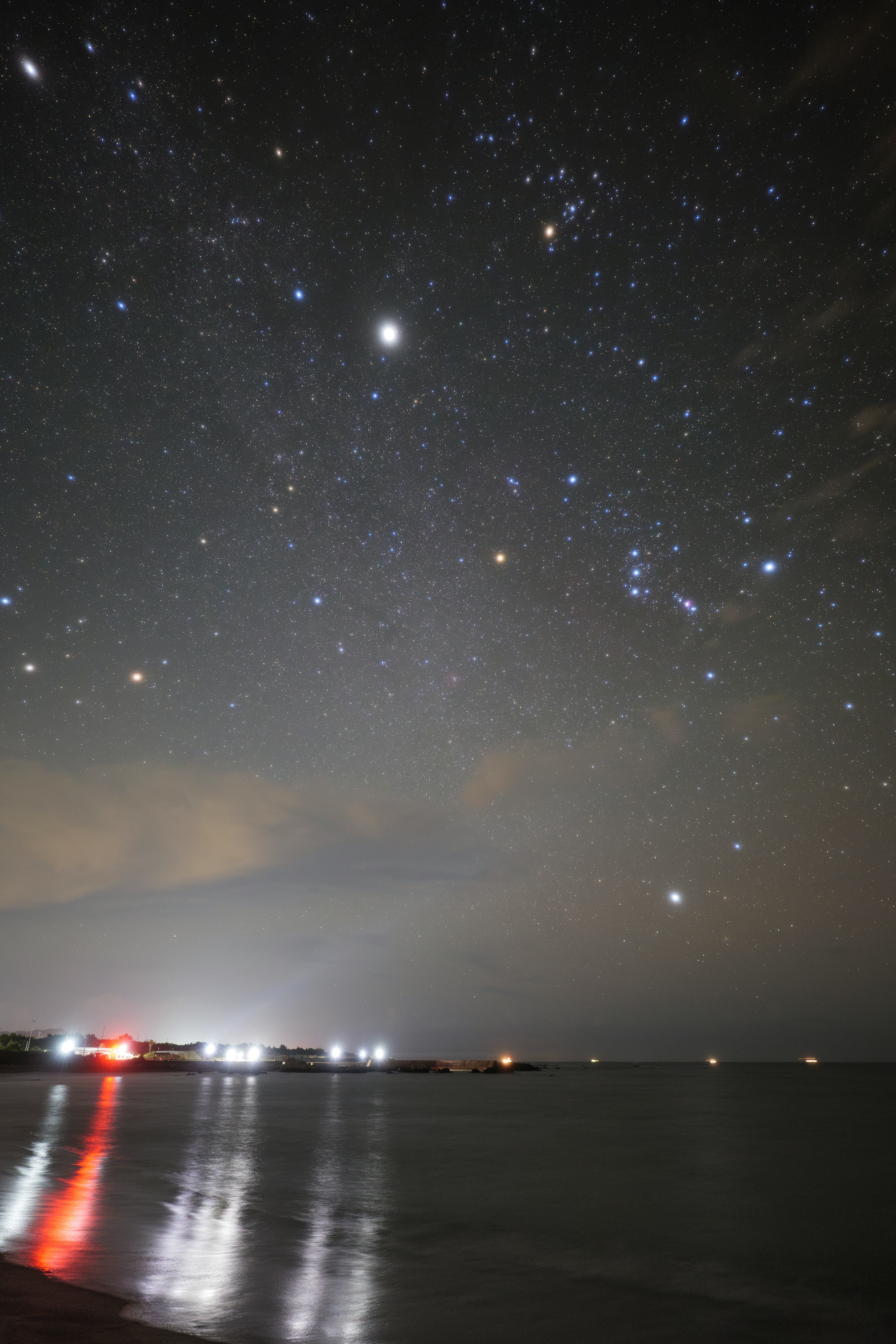 星空が広がる海岸の風景 光る星々と船の灯りが見える