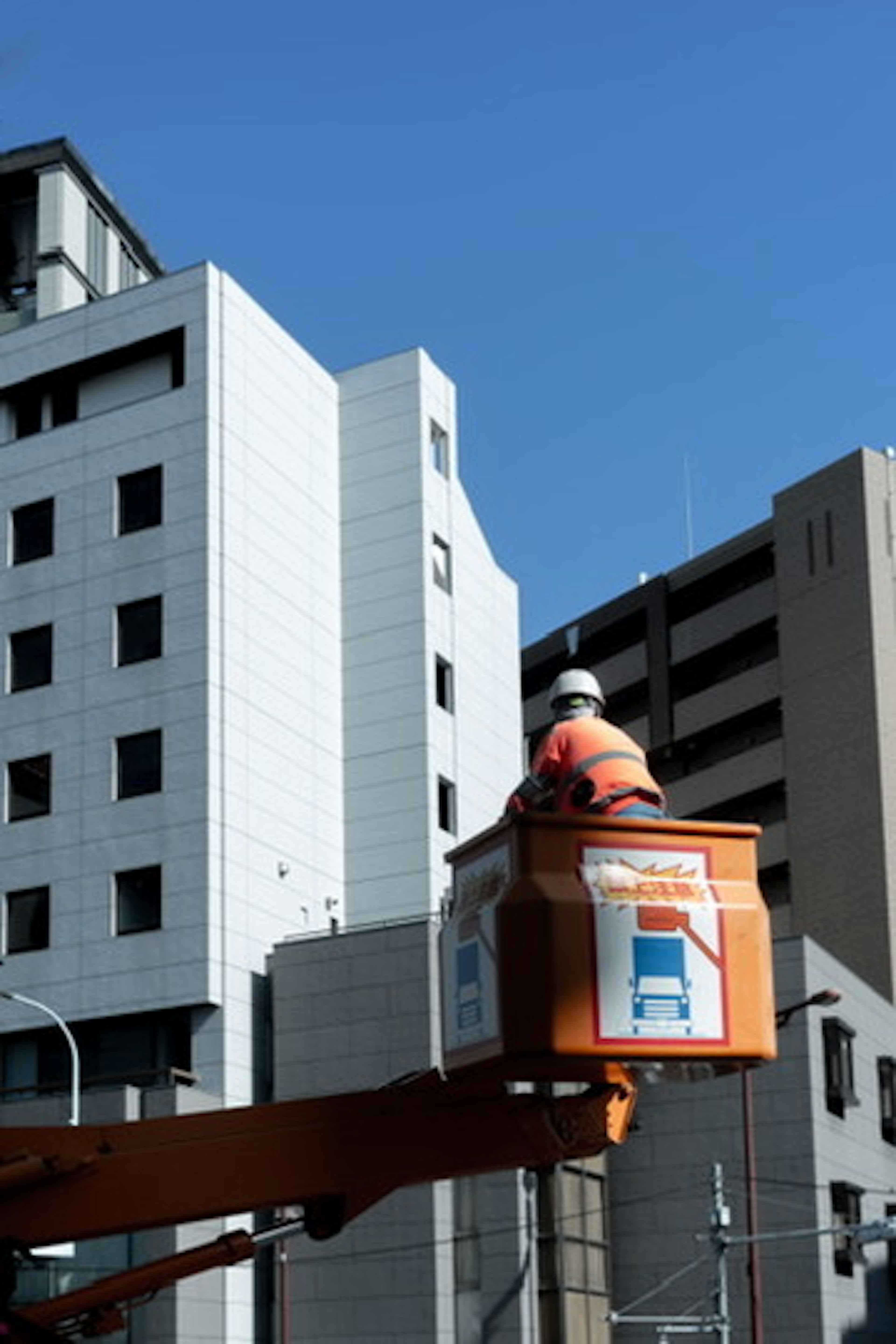 Worker in an orange bucket lift with modern buildings in the background