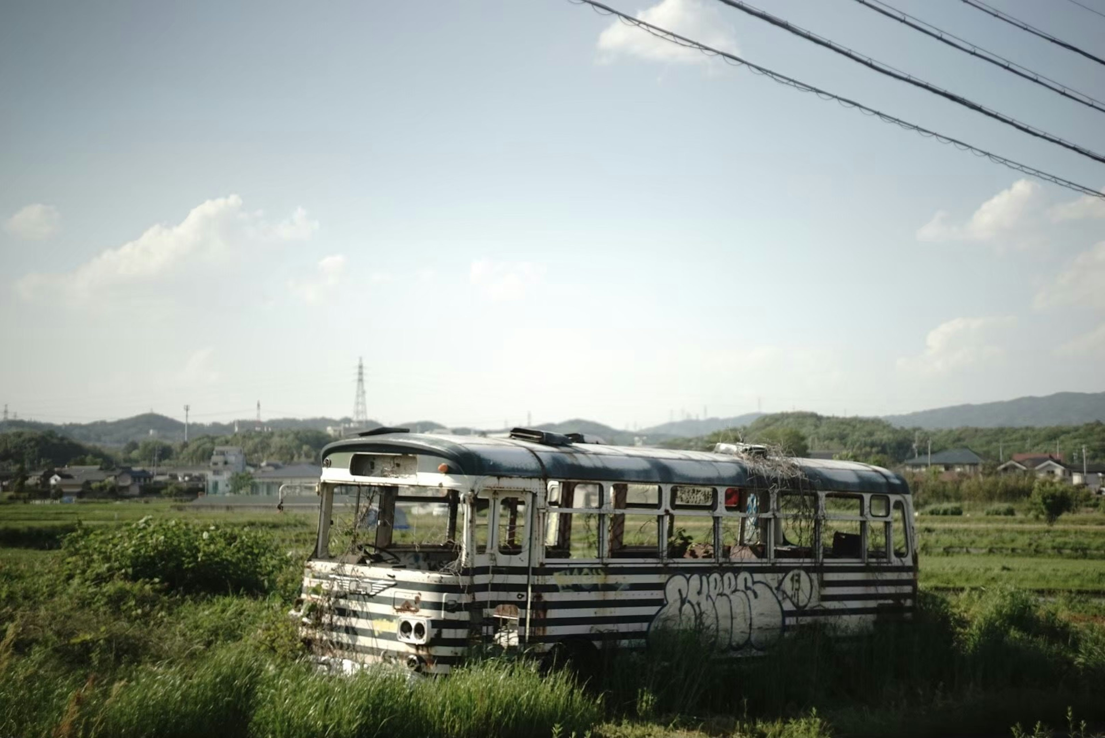 Abandoned bus vehicle overgrown with grass under blue sky