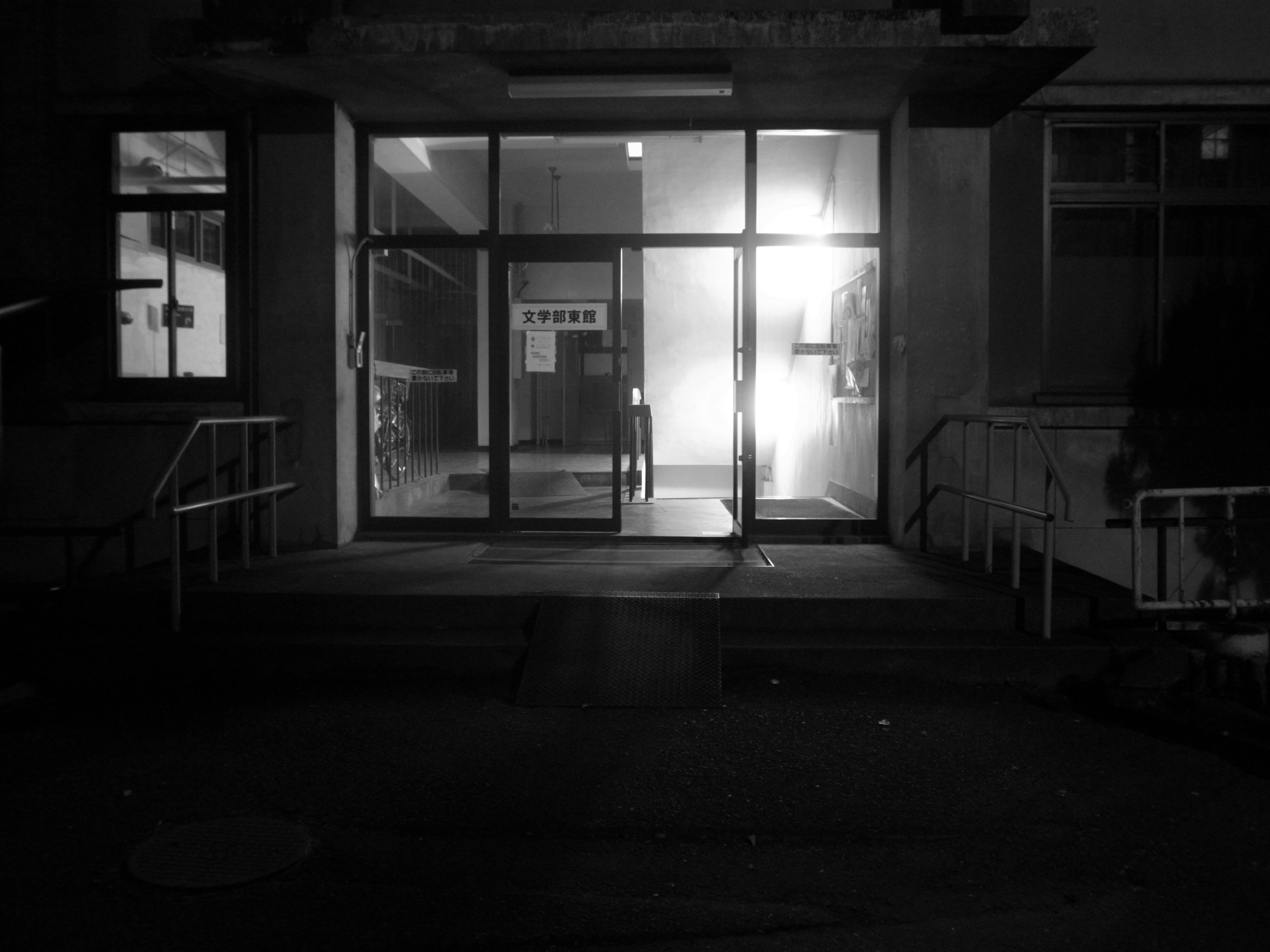 Entrance of a building with glass doors and lighting in a dark setting