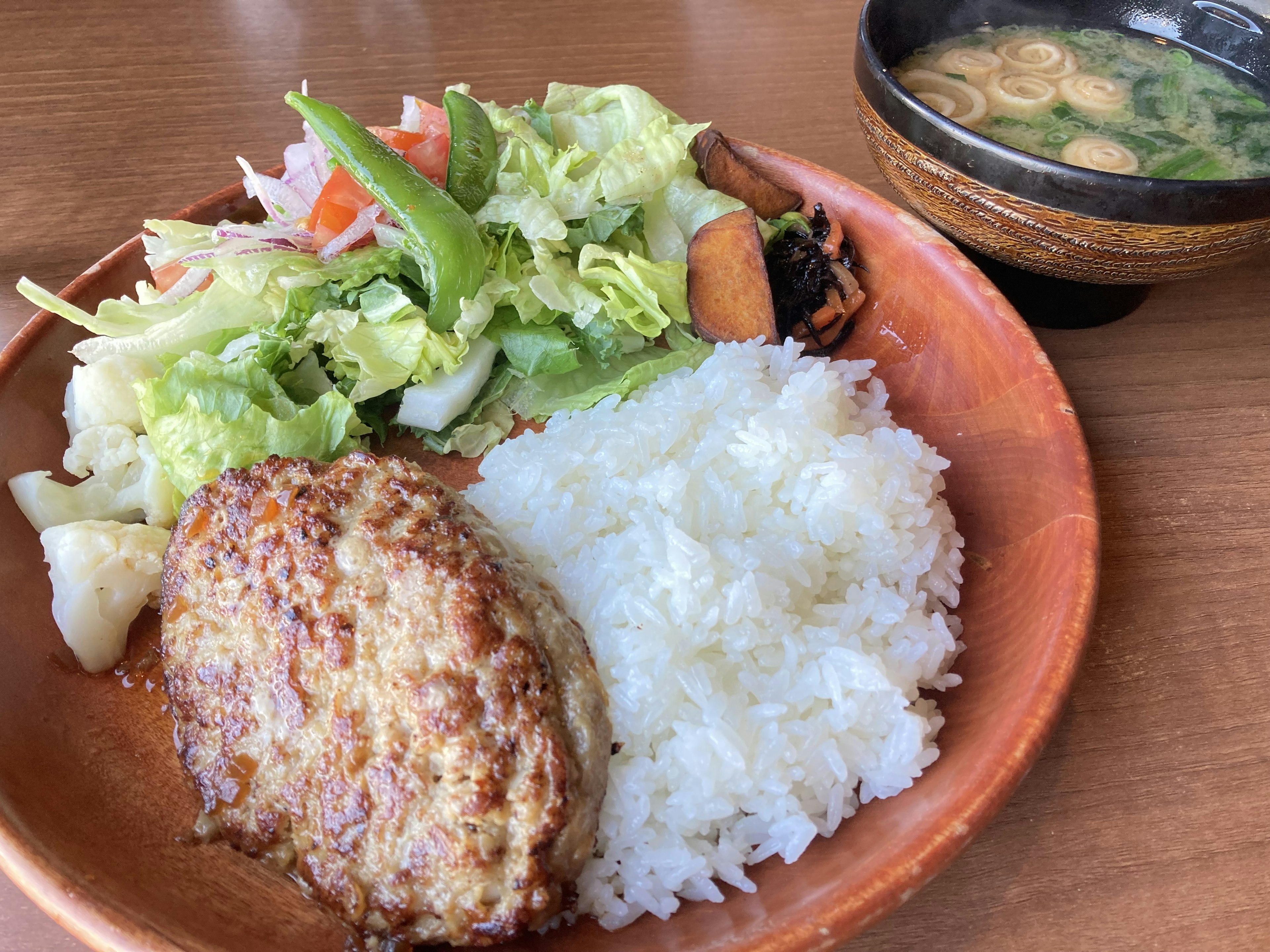 Une assiette avec un steak haché du riz blanc une salade fraîche et de la soupe miso