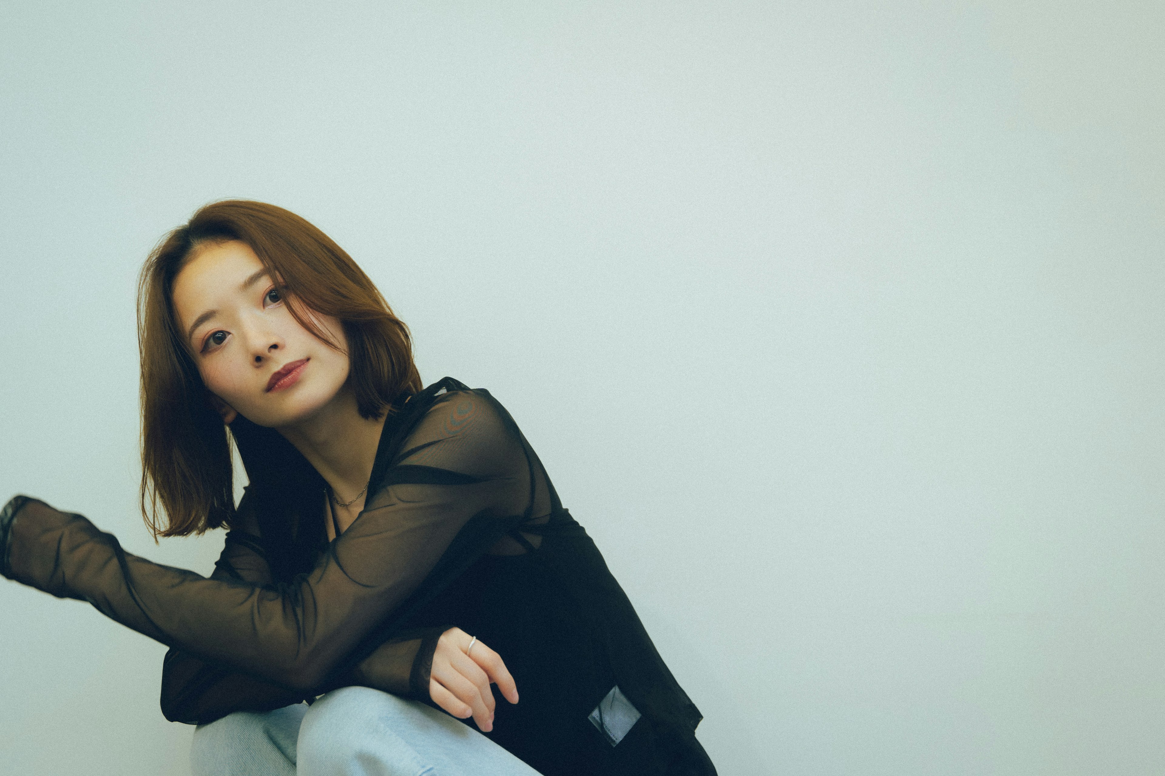 Portrait d'une femme assise contre un fond simple portant un haut noir et un jean les cheveux tombant sur ses épaules