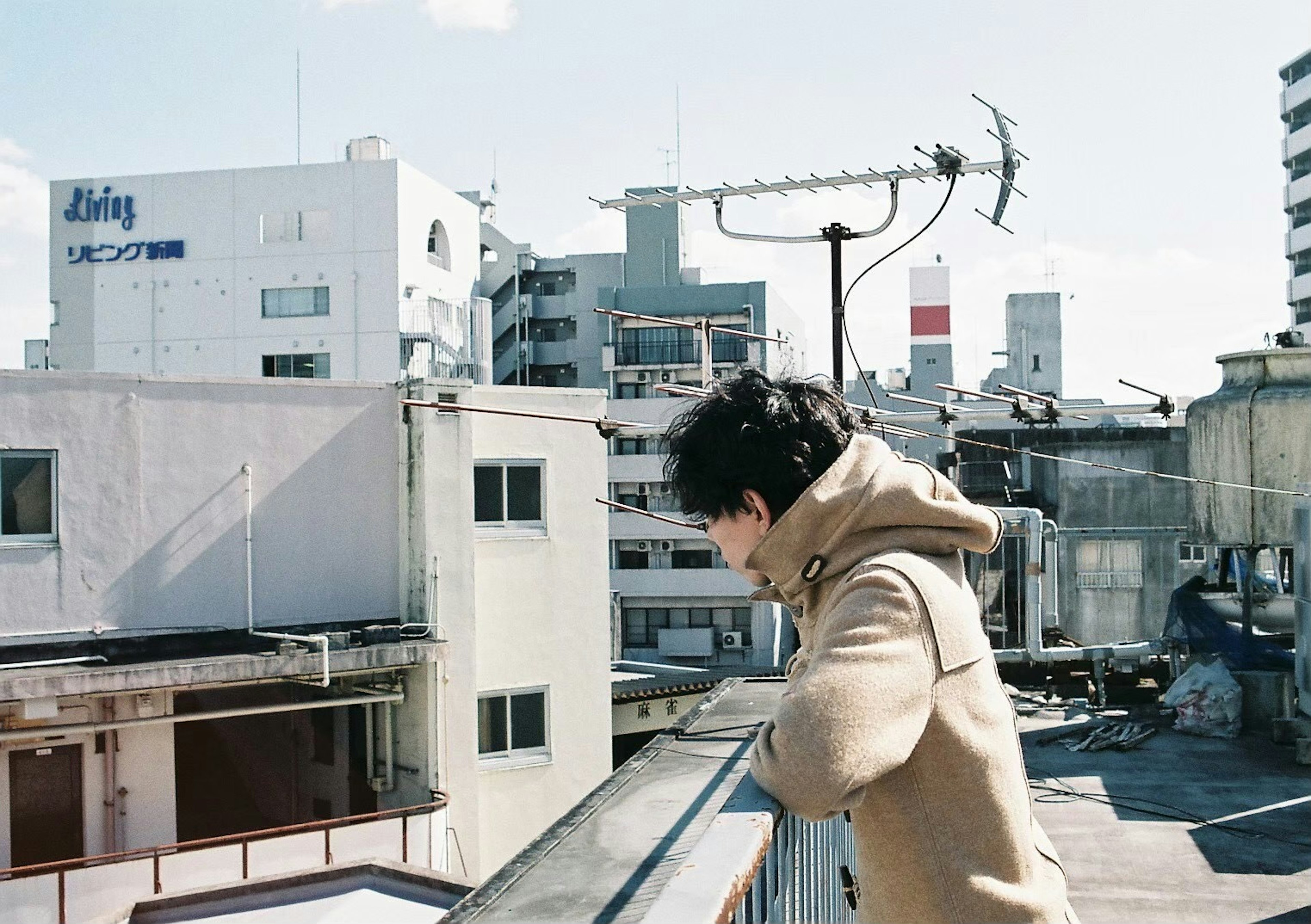 Young man standing on a rooftop in the city with buildings and antennas in the background