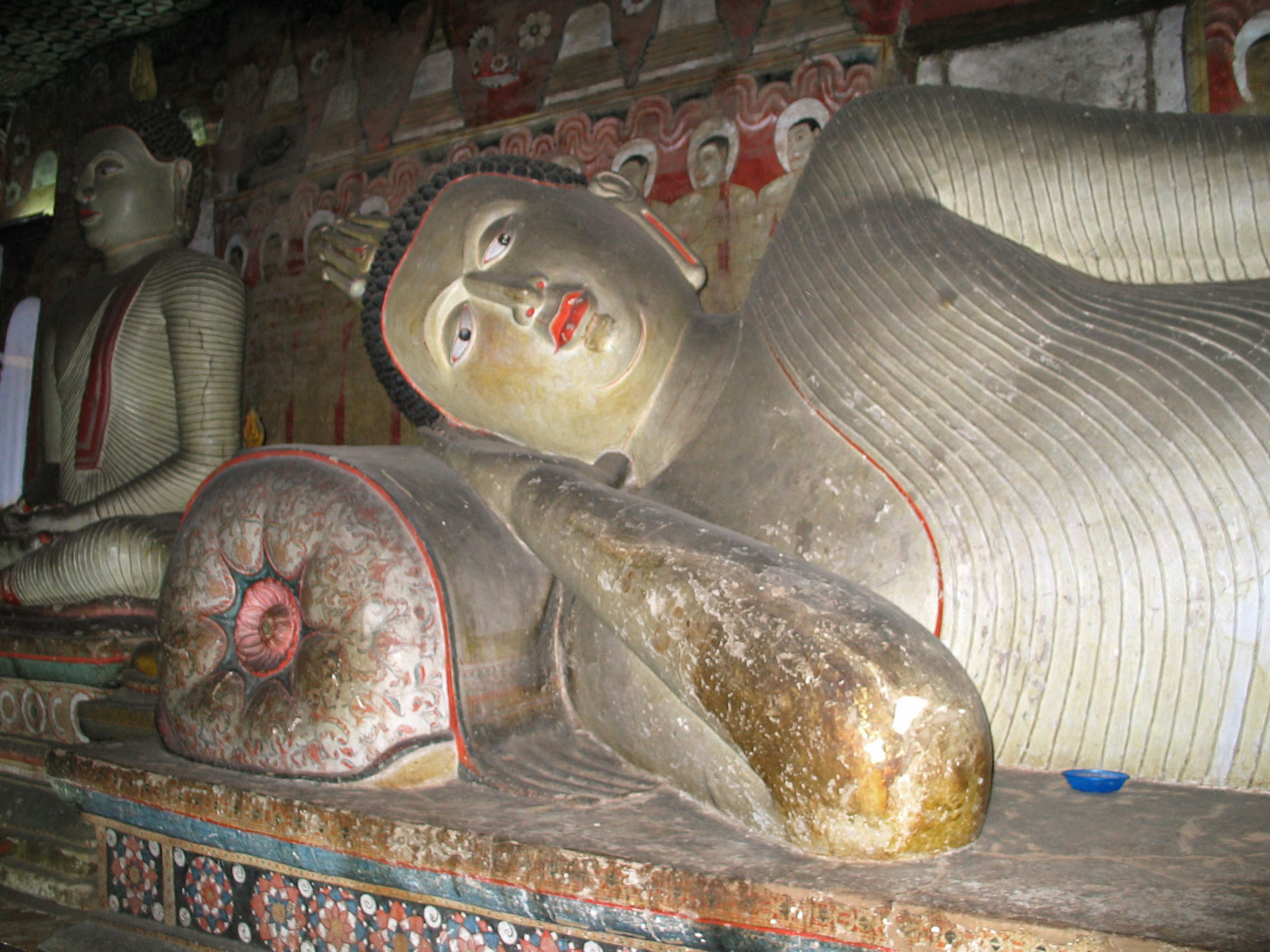 Statue de Bouddha couché avec des peintures murales anciennes dans un intérieur de grotte