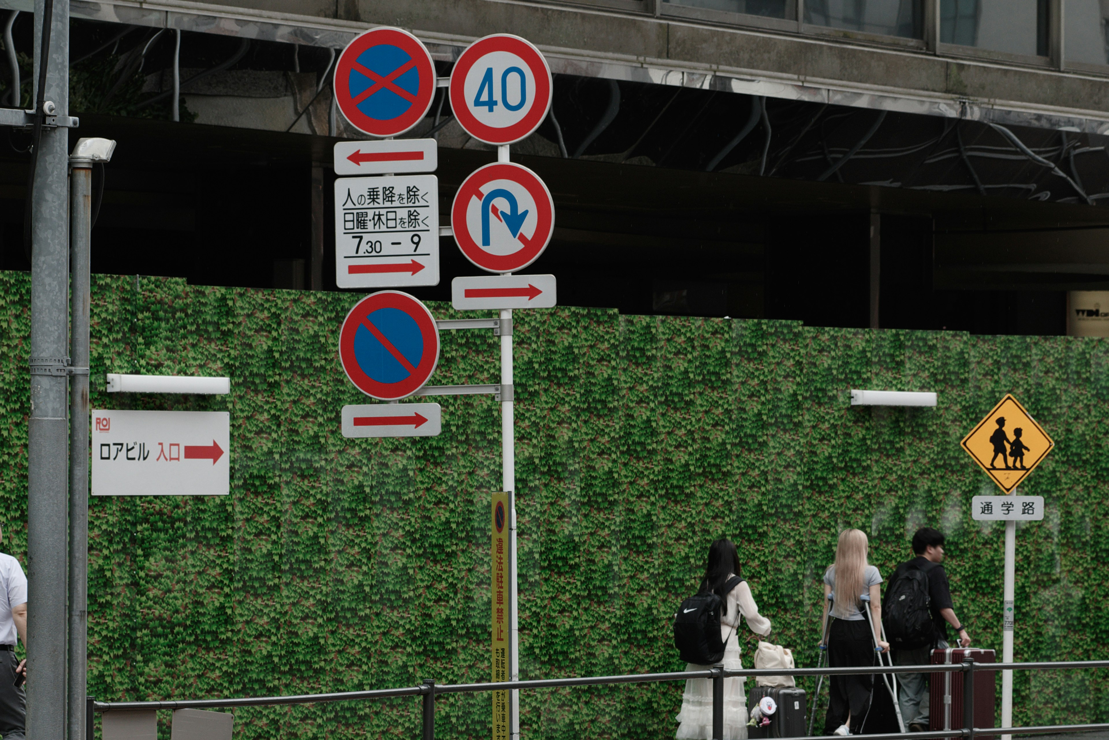 Segnali stradali davanti a un muro verde con pedoni