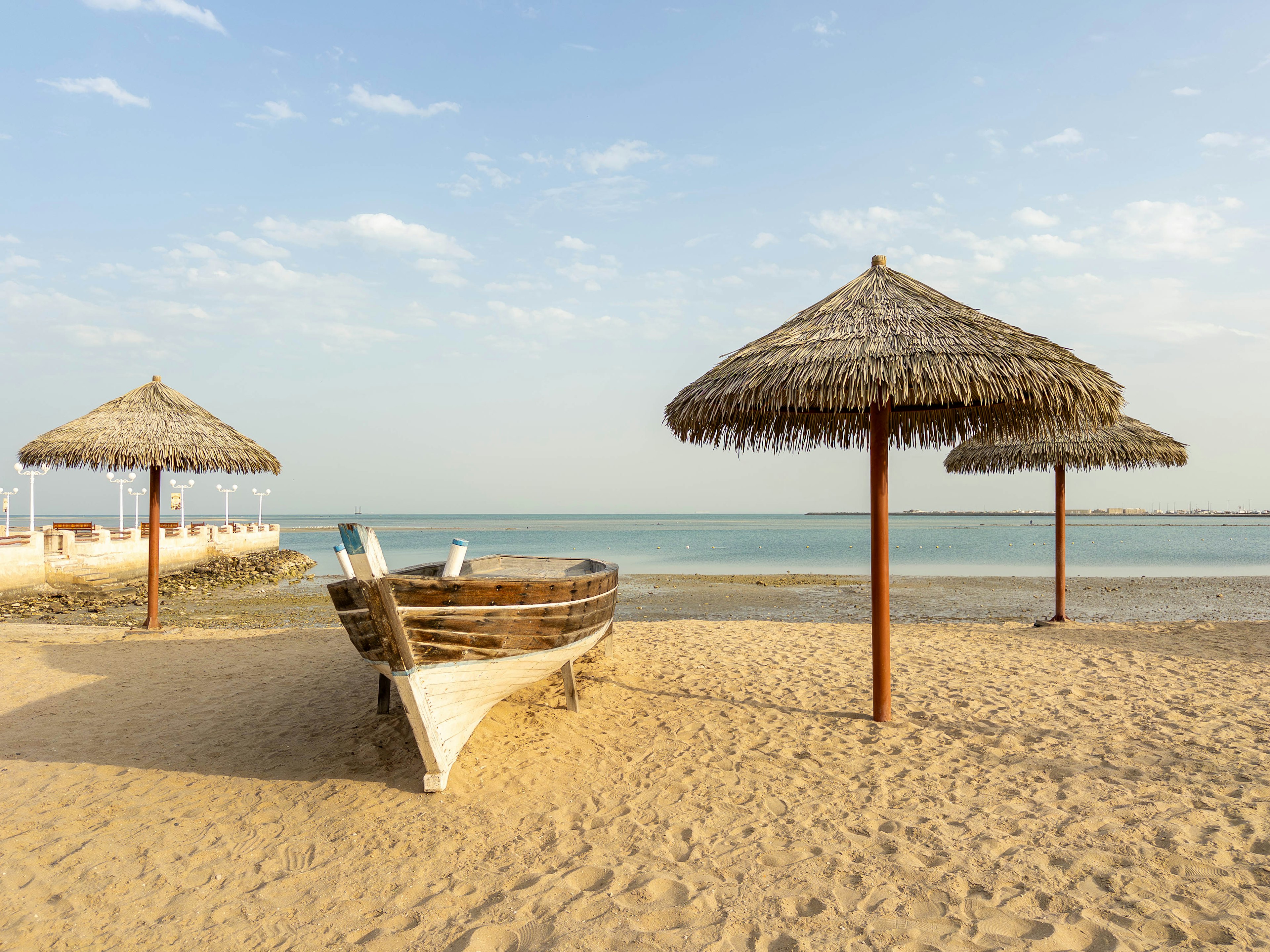 Holzboot und Strohdächer an einem Sandstrand