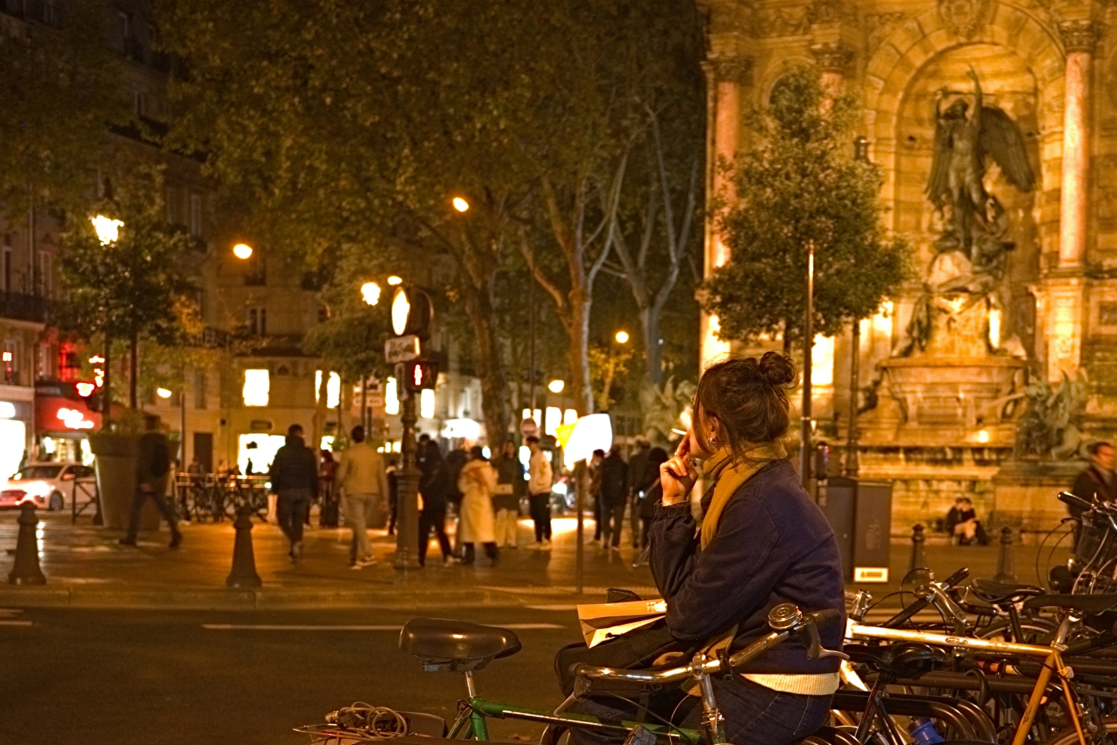 Una mujer sentada en una bicicleta en una plaza de París por la noche con una escena de calle animada