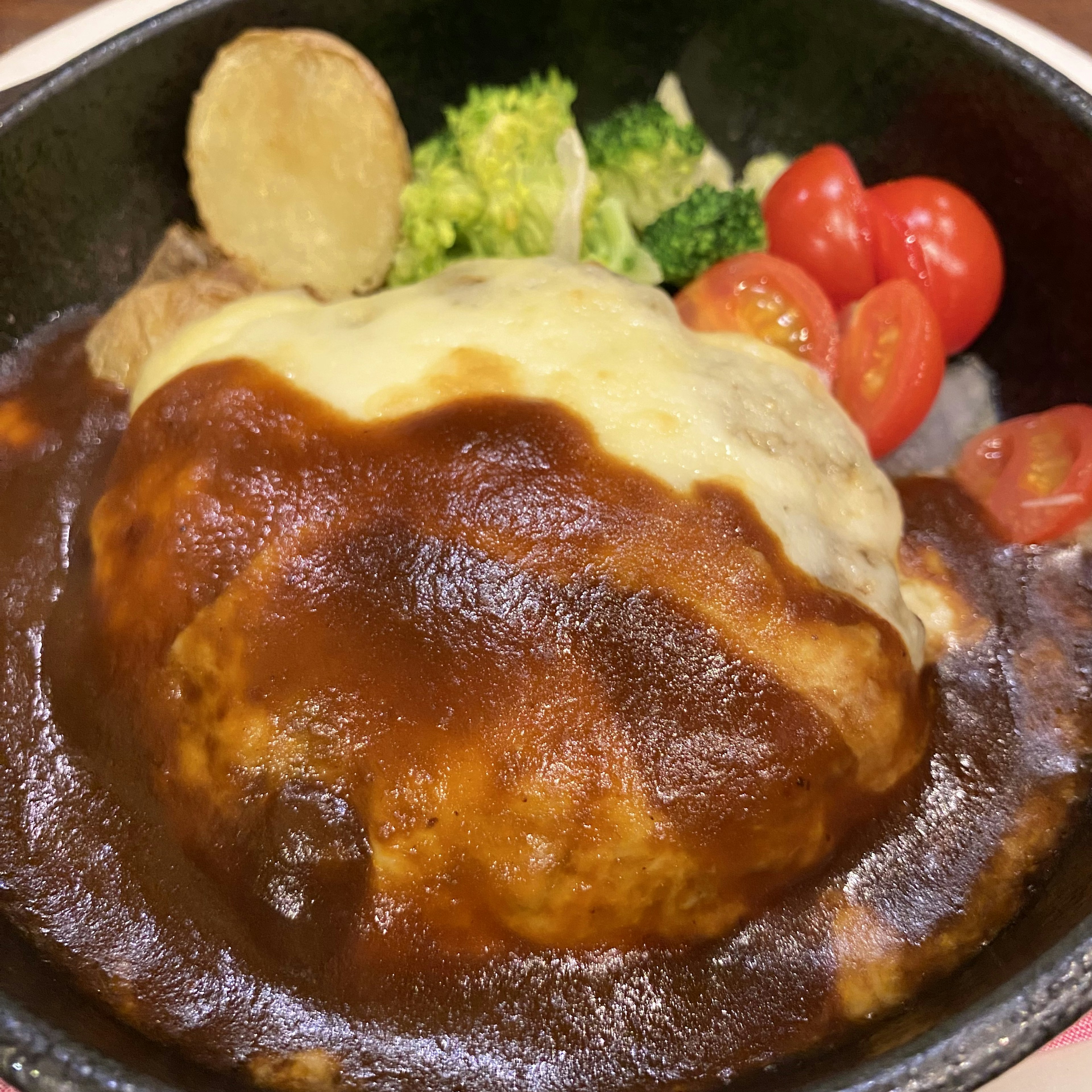 Ein Hamburgersteak mit geschmolzenem Käse und reichhaltiger Demi-Glace-Sauce serviert mit Gemüse