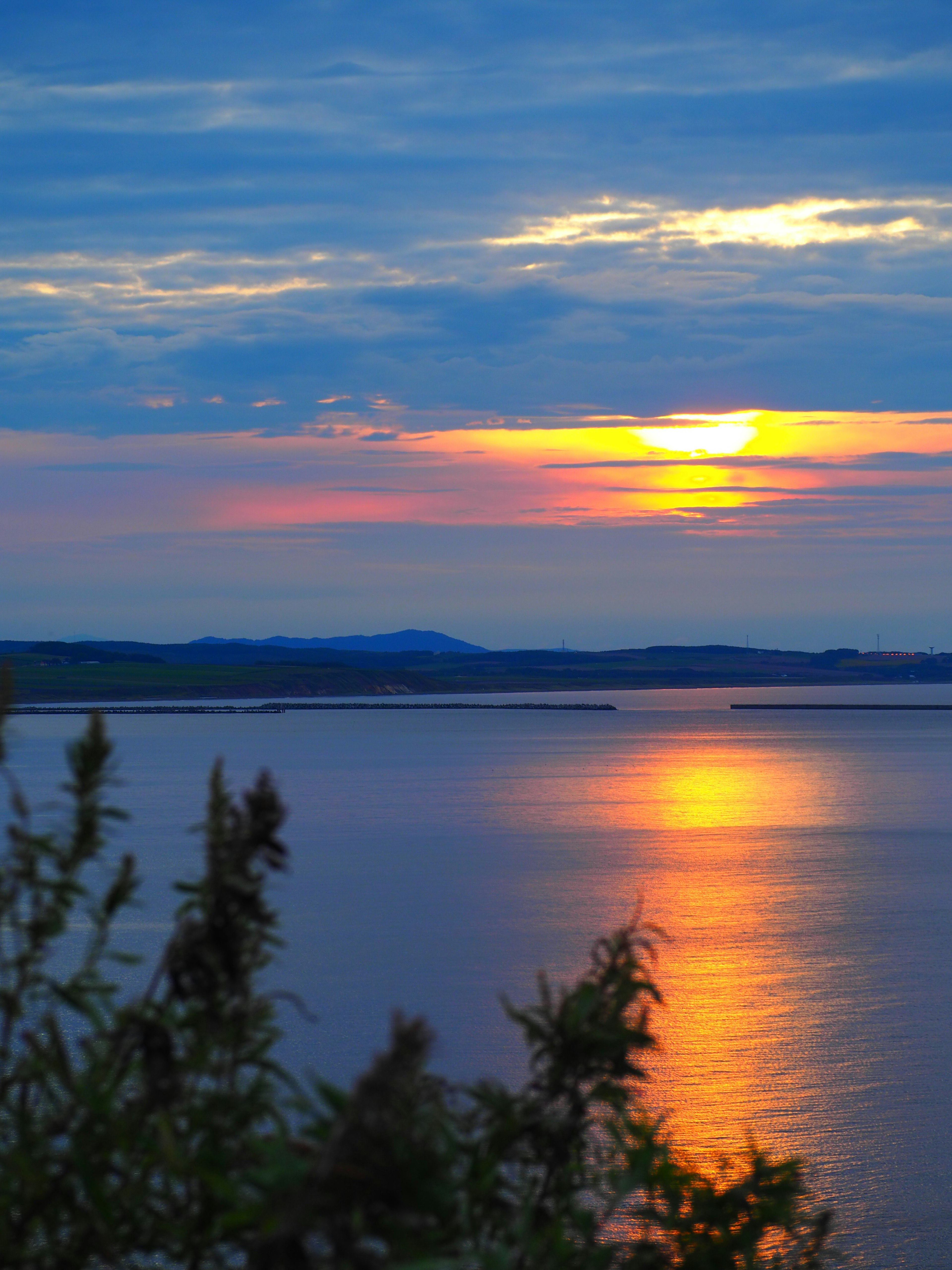 Malersicher Blick auf einen See bei Sonnenuntergang mit lebendigen orange und blauen Farben, die sich im Wasser spiegeln