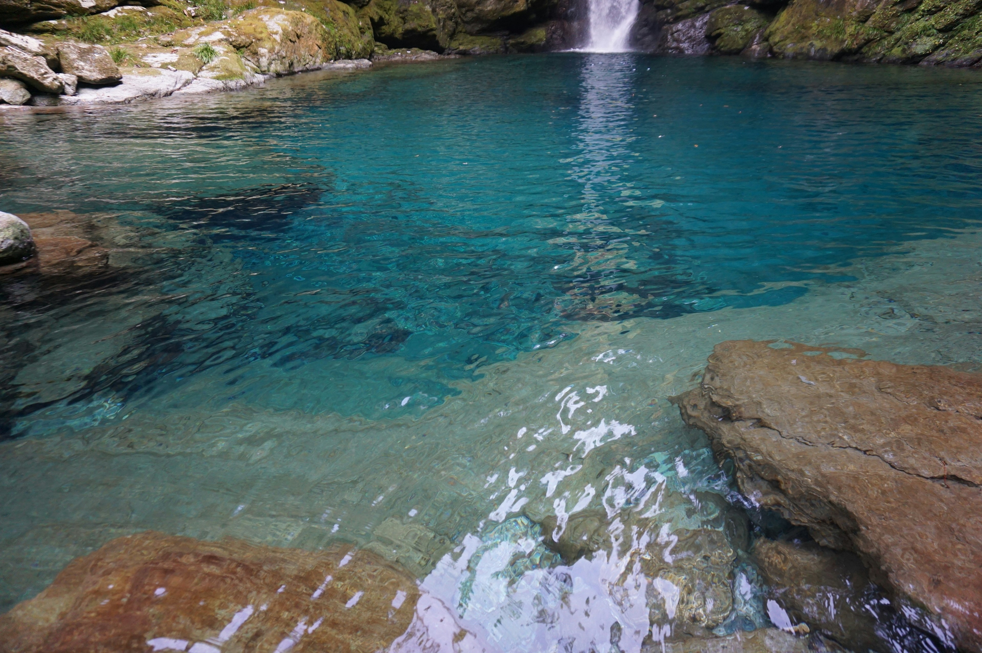 Agua clara y azul con rocas y una cascada al fondo