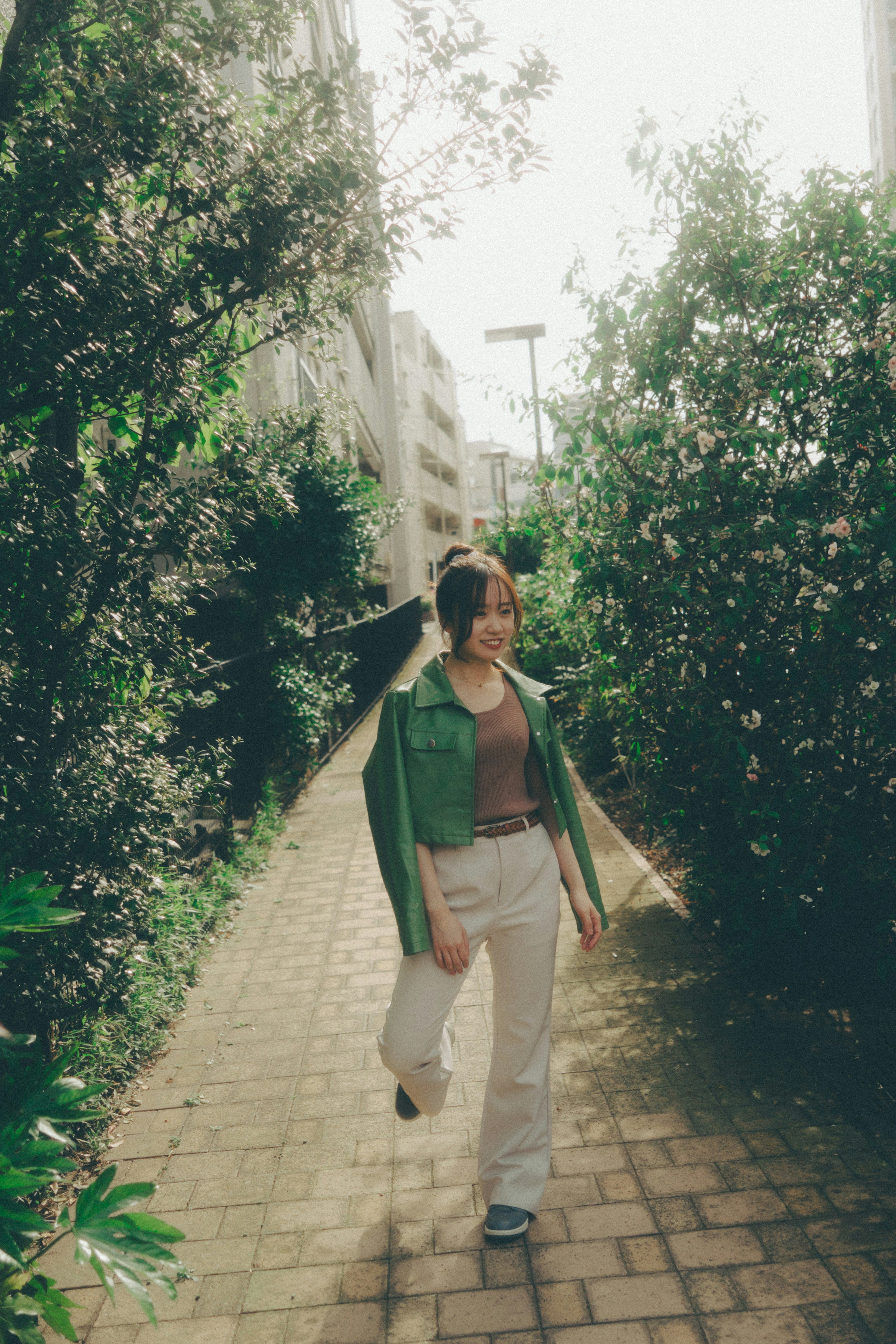 A woman in a green jacket walking along a path surrounded by greenery