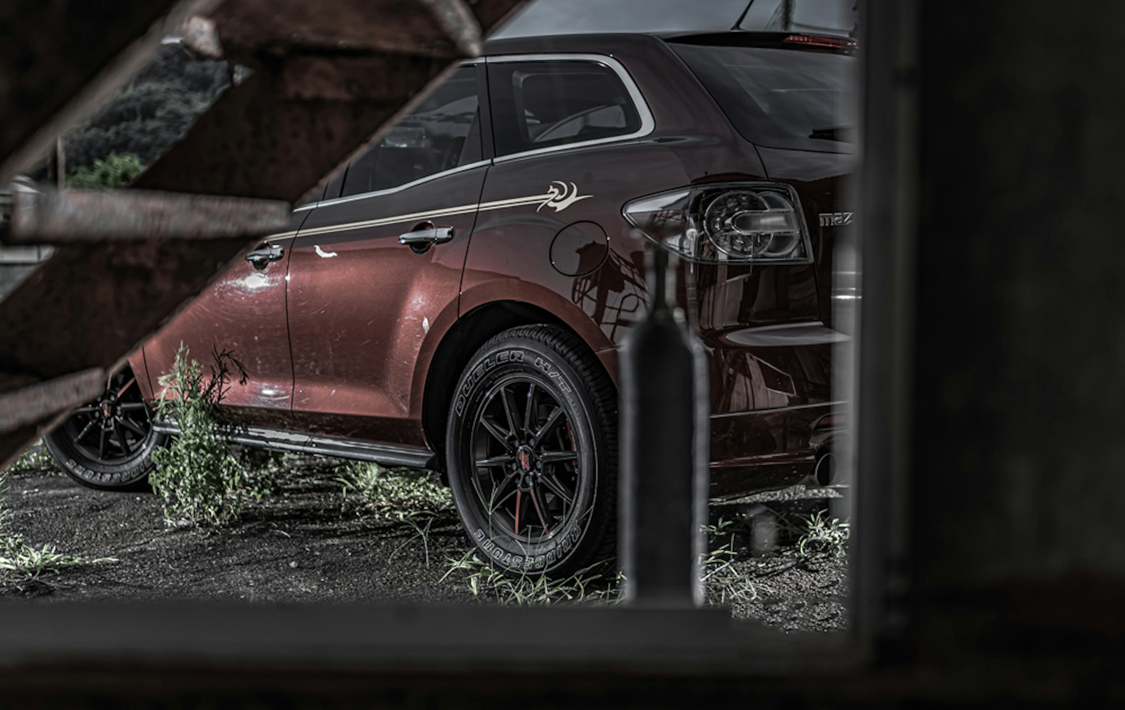 Vista lateral de un coche deportivo rojo con ruedas negras en un entorno abandonado