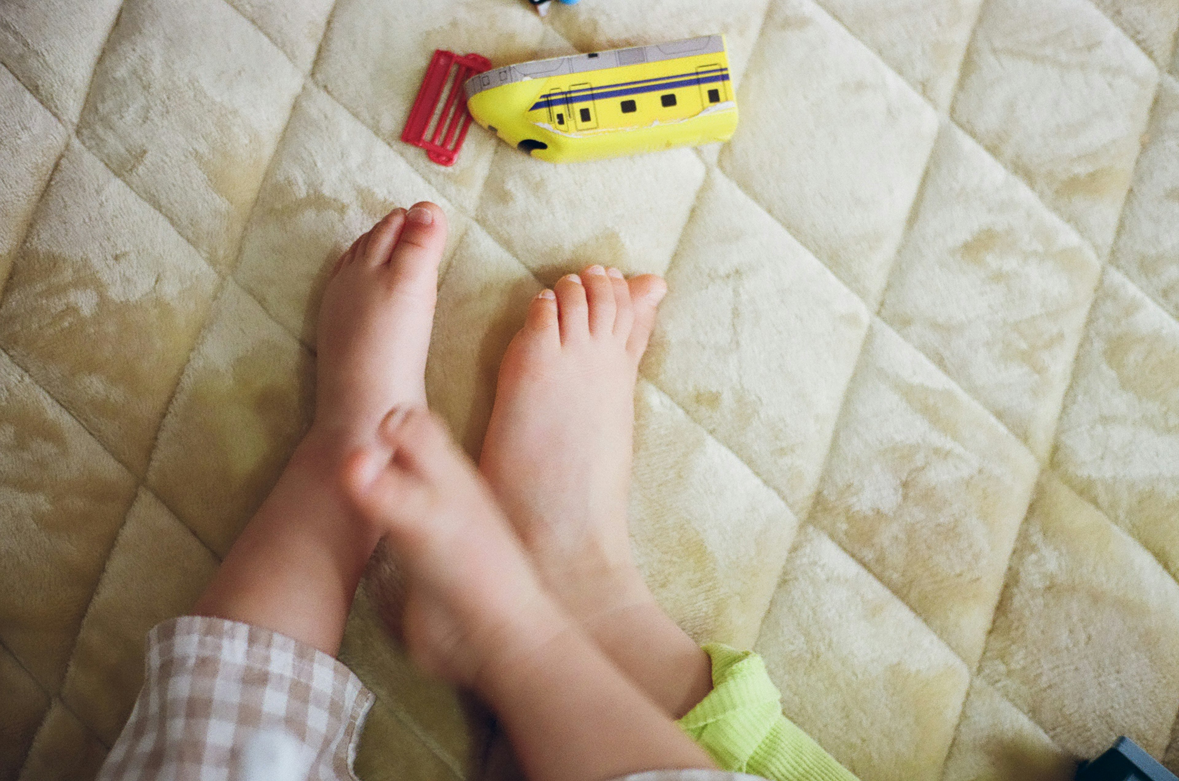 Pies de niños con un submarino de juguete amarillo sobre una cama acolchada