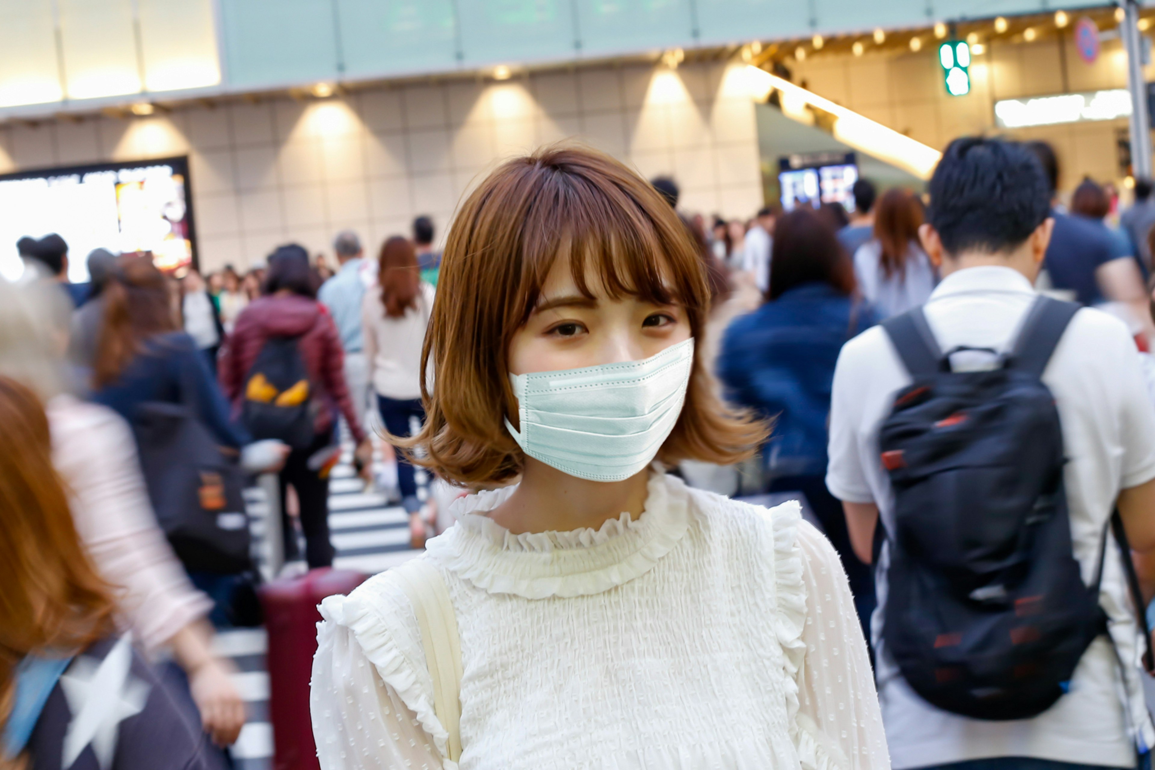 A woman wearing a mask smiles in a crowded area