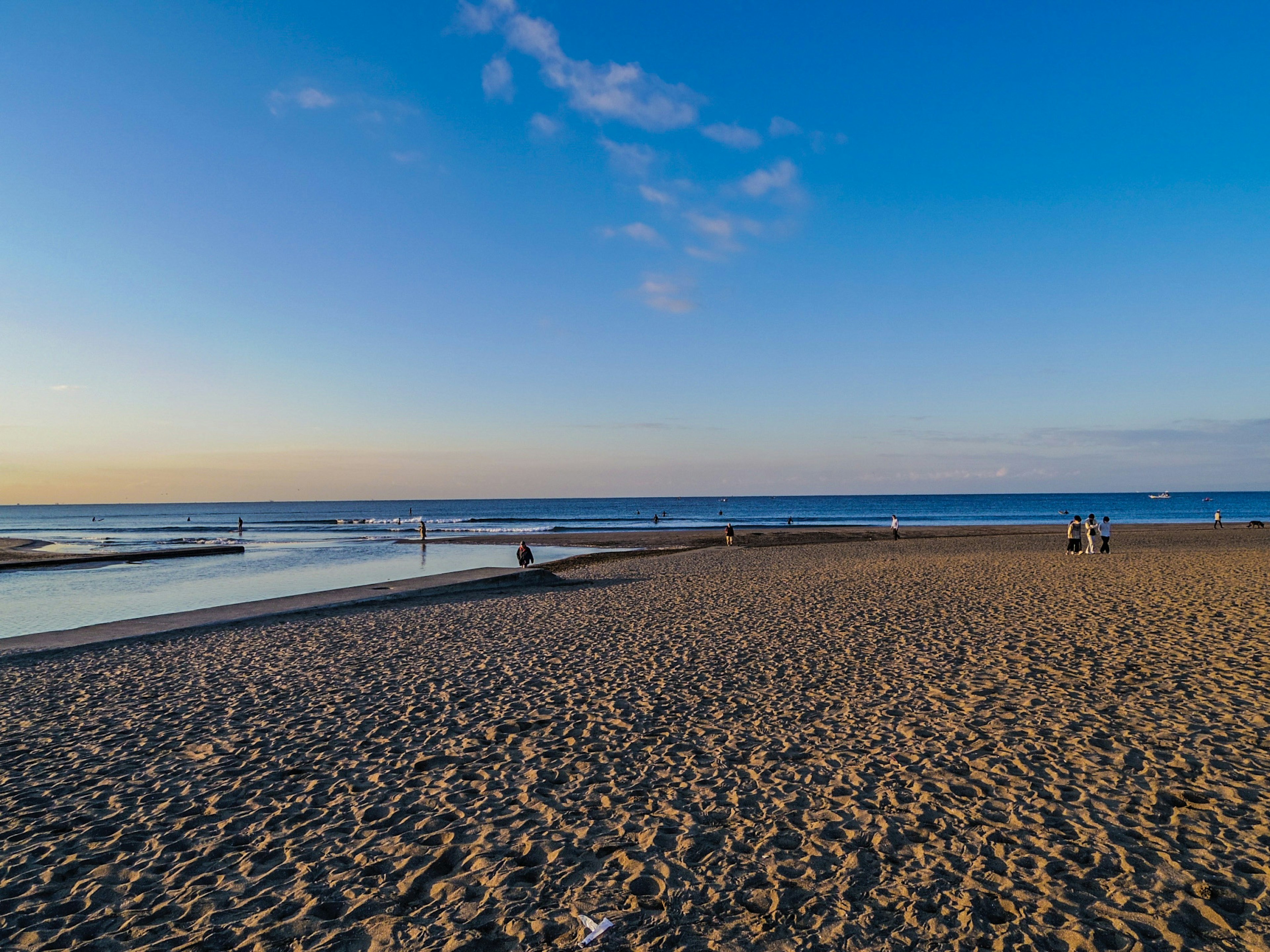 ภาพชายหาดที่มีท้องฟ้าสีฟ้าและมหาสมุทร ทรายที่มีผู้คนและวัตถุกระจัดกระจาย