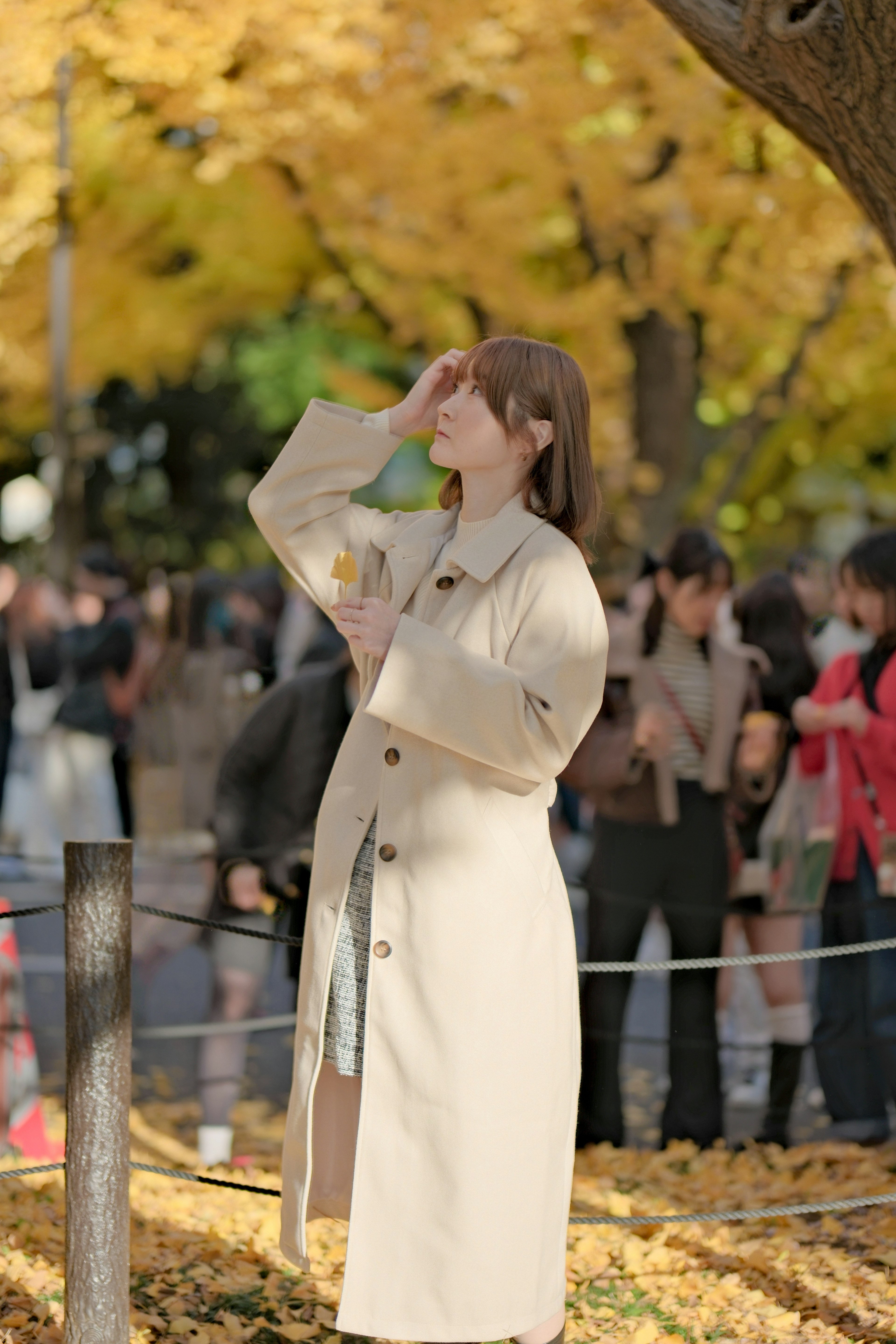 秋の公園で黄色い葉の中に立つ女性の姿