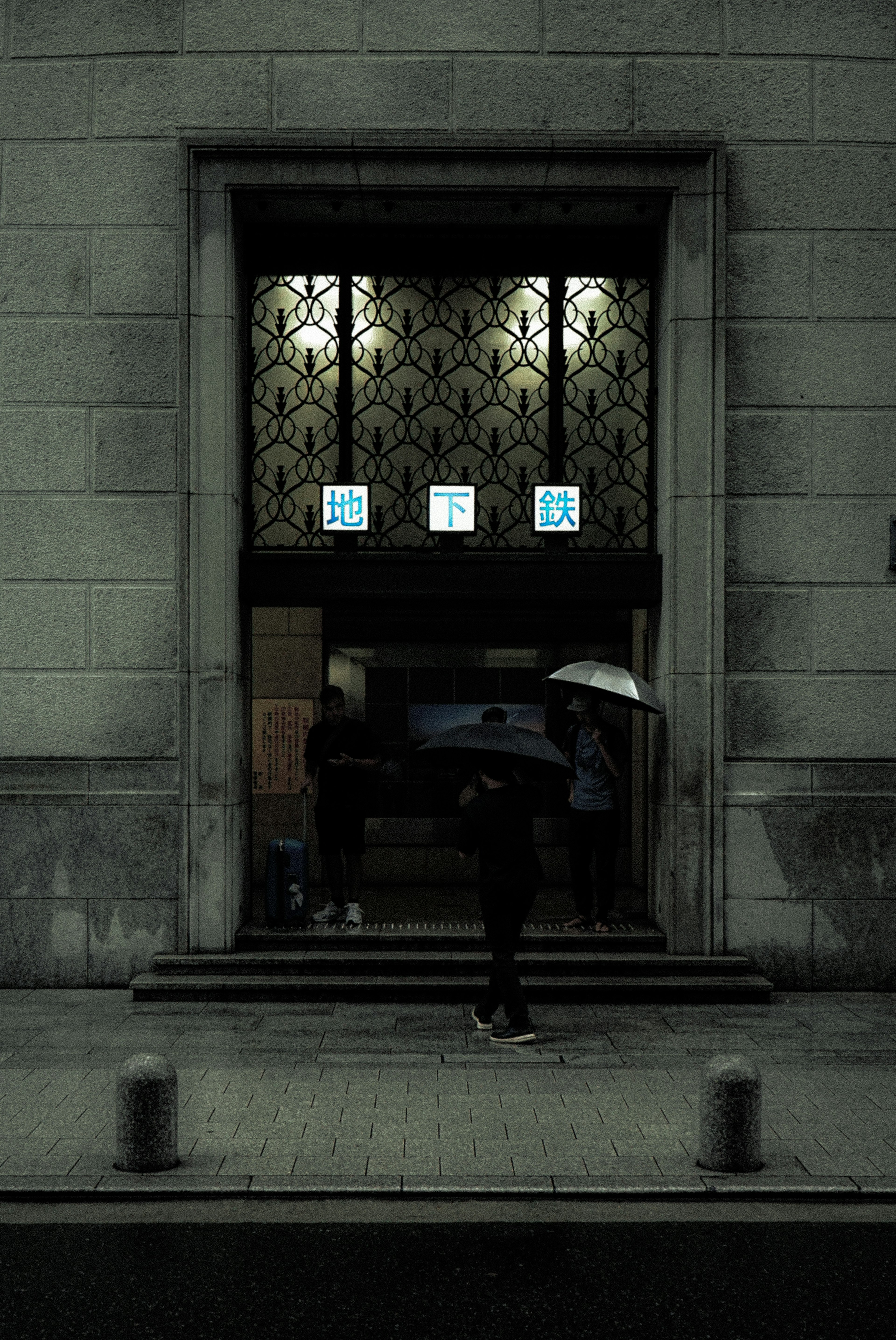 A person with an umbrella walking in front of a beautiful building entrance on a dark street