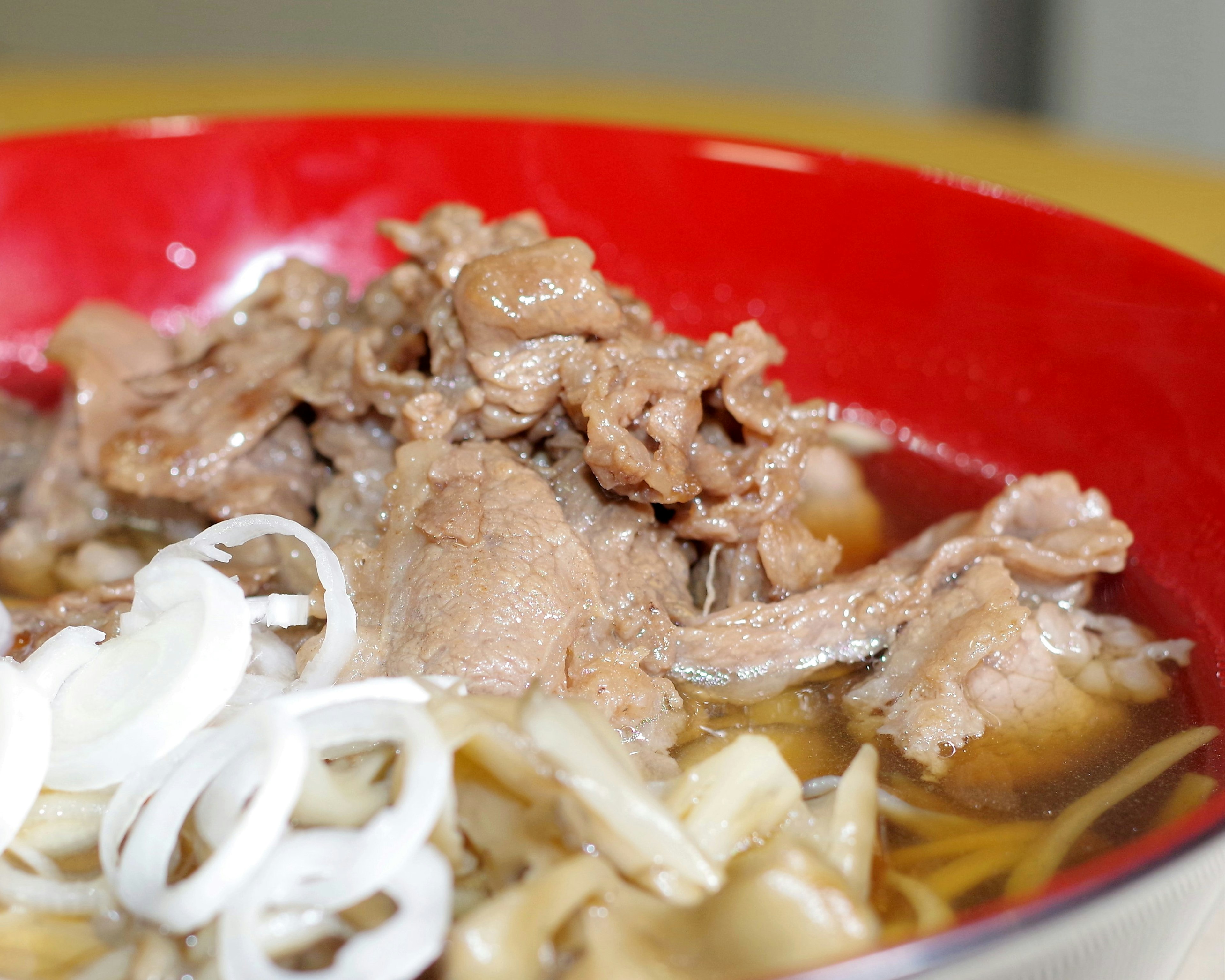 Ramen disajikan dalam mangkuk merah dengan daging dan irisan bawang hijau