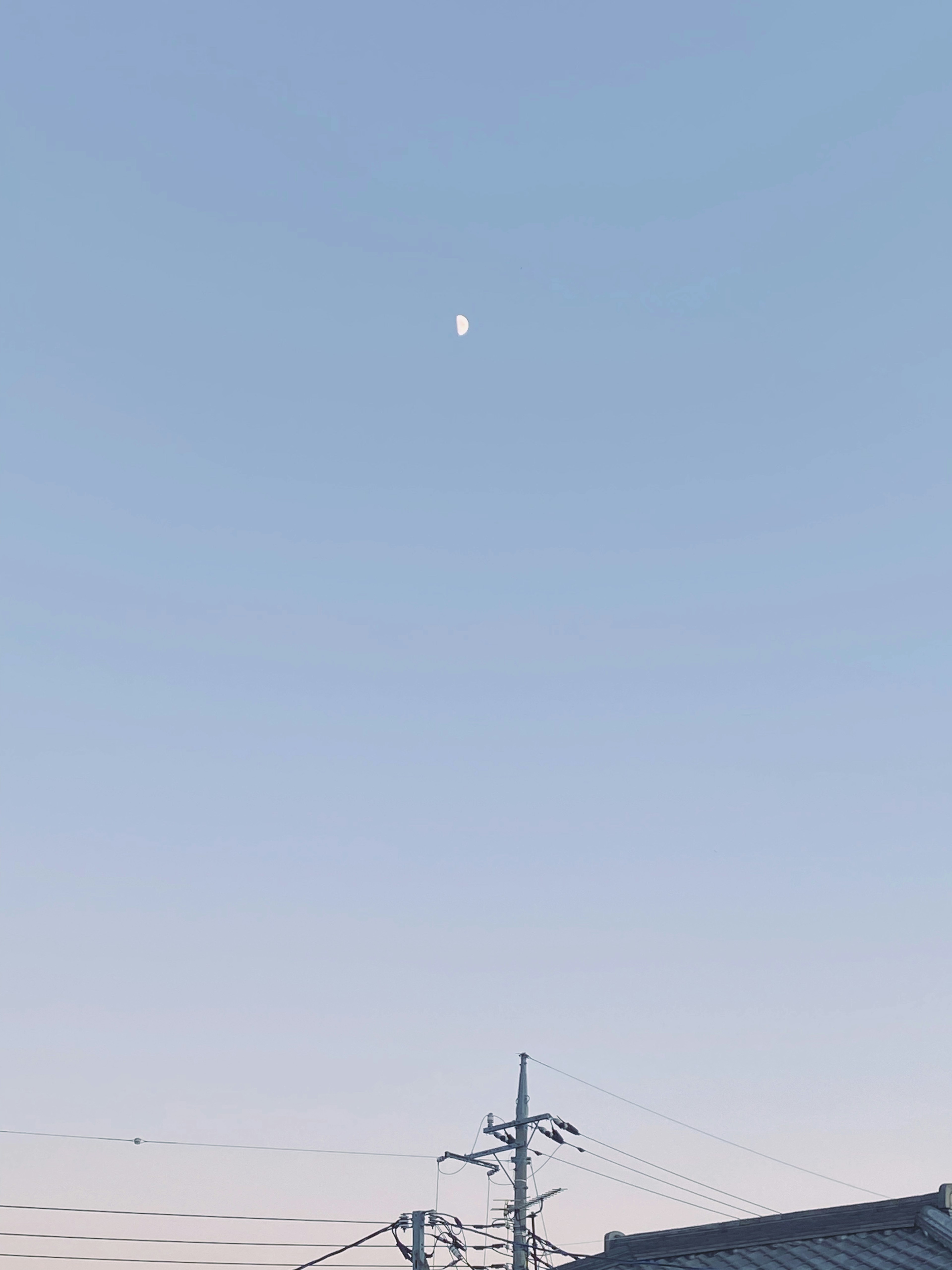 Moon in a clear blue sky with power lines