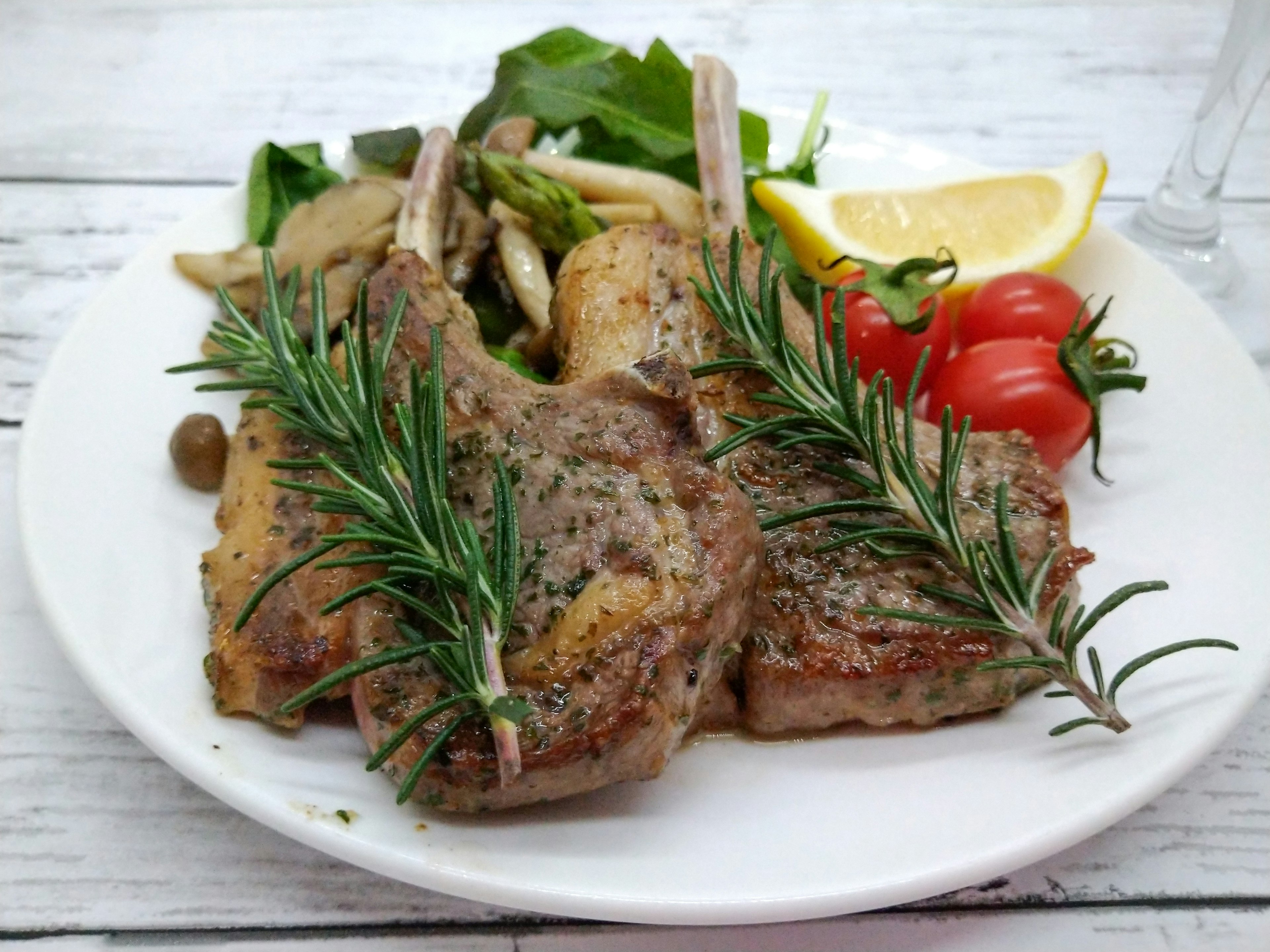 Côtelettes d'agneau grillées garnies de romarin servies avec une salade et un citron