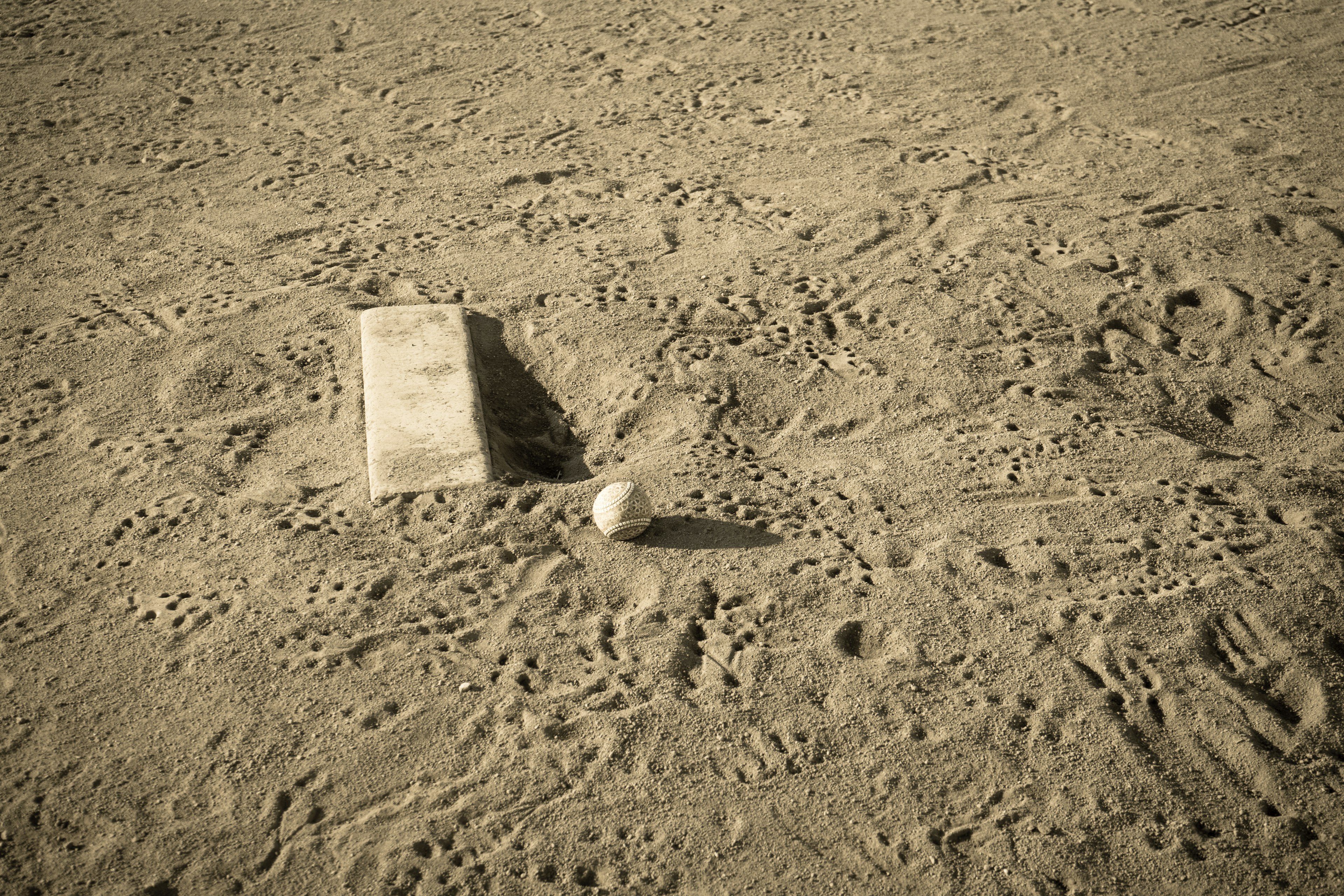 A baseball and a base sitting on a sandy surface