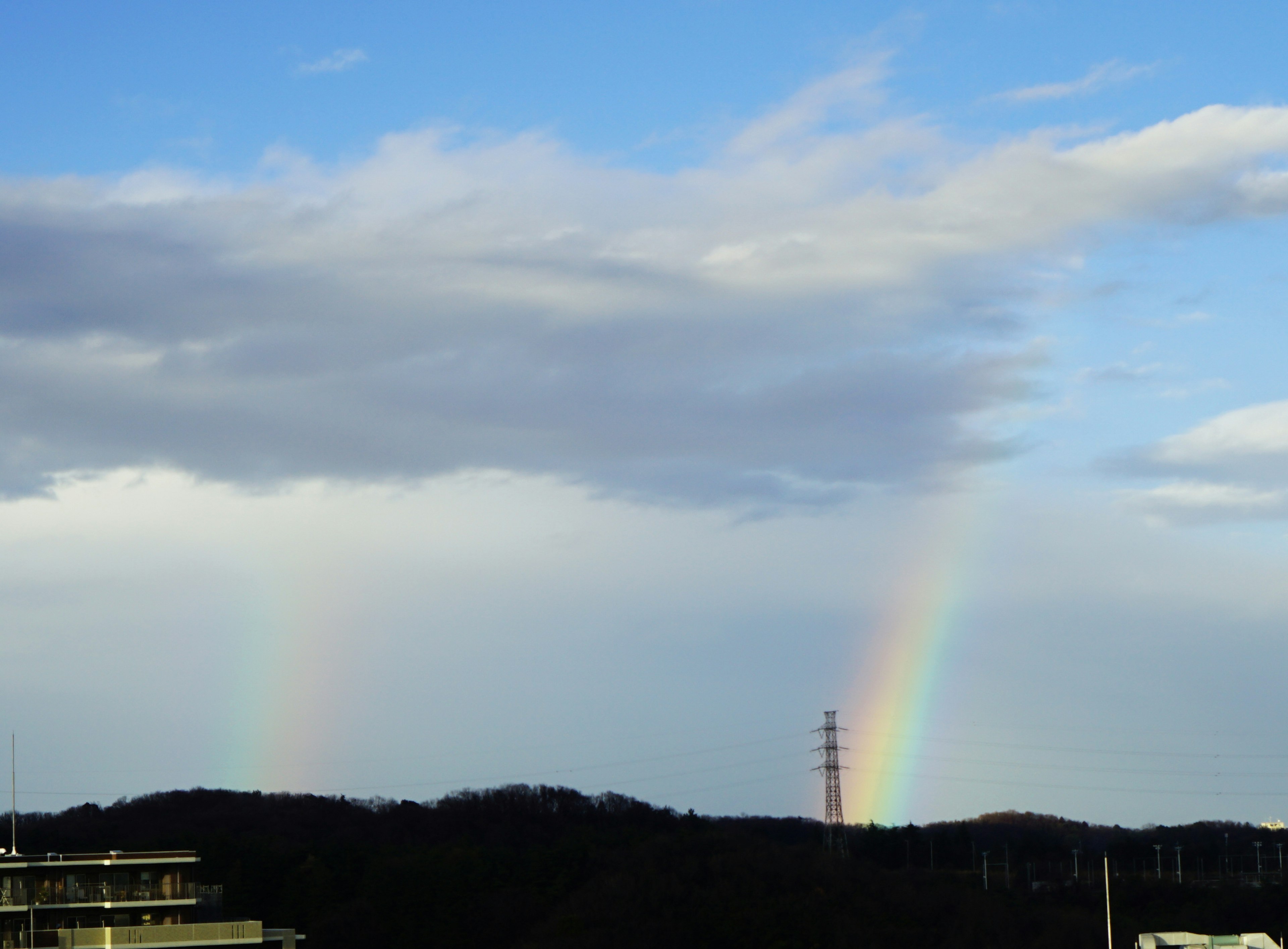 Un paesaggio con un arcobaleno che attraversa un cielo blu con nuvole