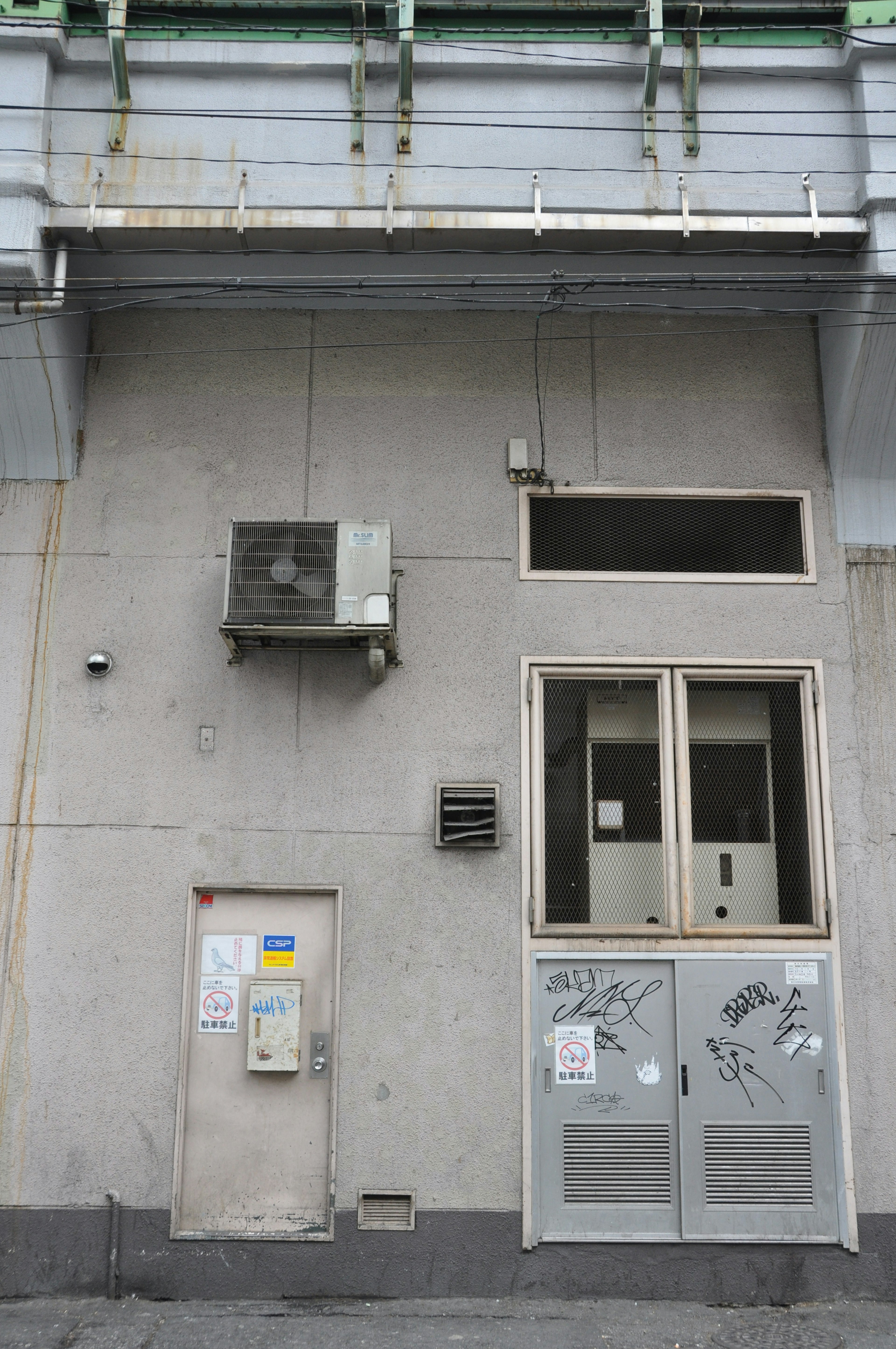 Façade d'un bâtiment avec un mur gris une unité de climatisation et une petite fenêtre