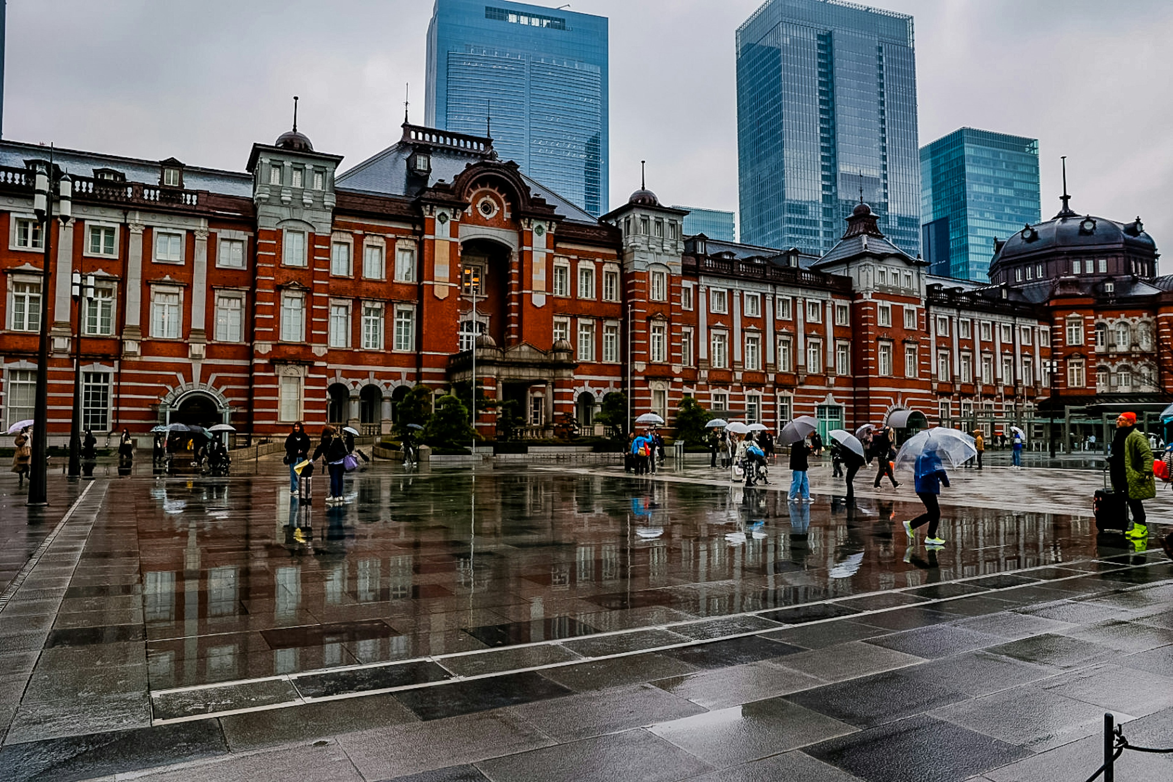 東京駅の歴史的な建物と現代の高層ビルが映る雨の日の風景