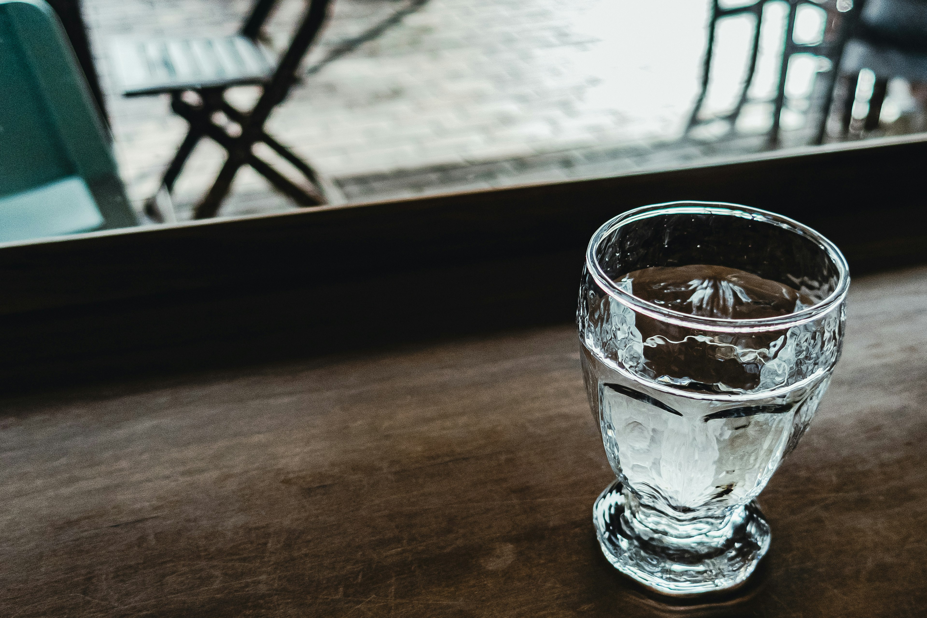 A clear glass of water on a wooden table with blurred chairs in the background