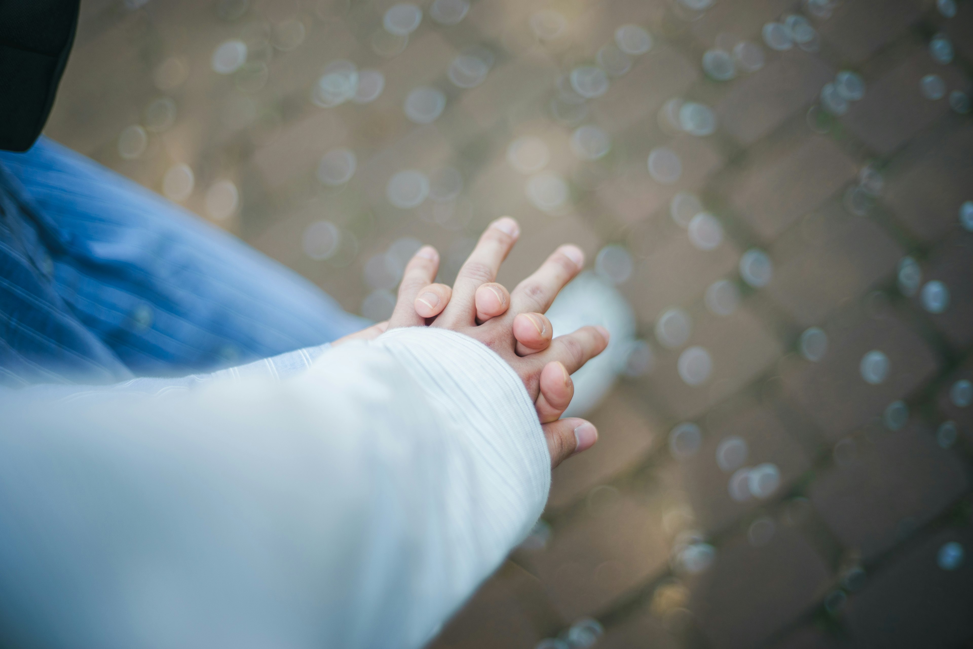 Close-up of two hands holding each other with flower petals scattered on the paved path in the background