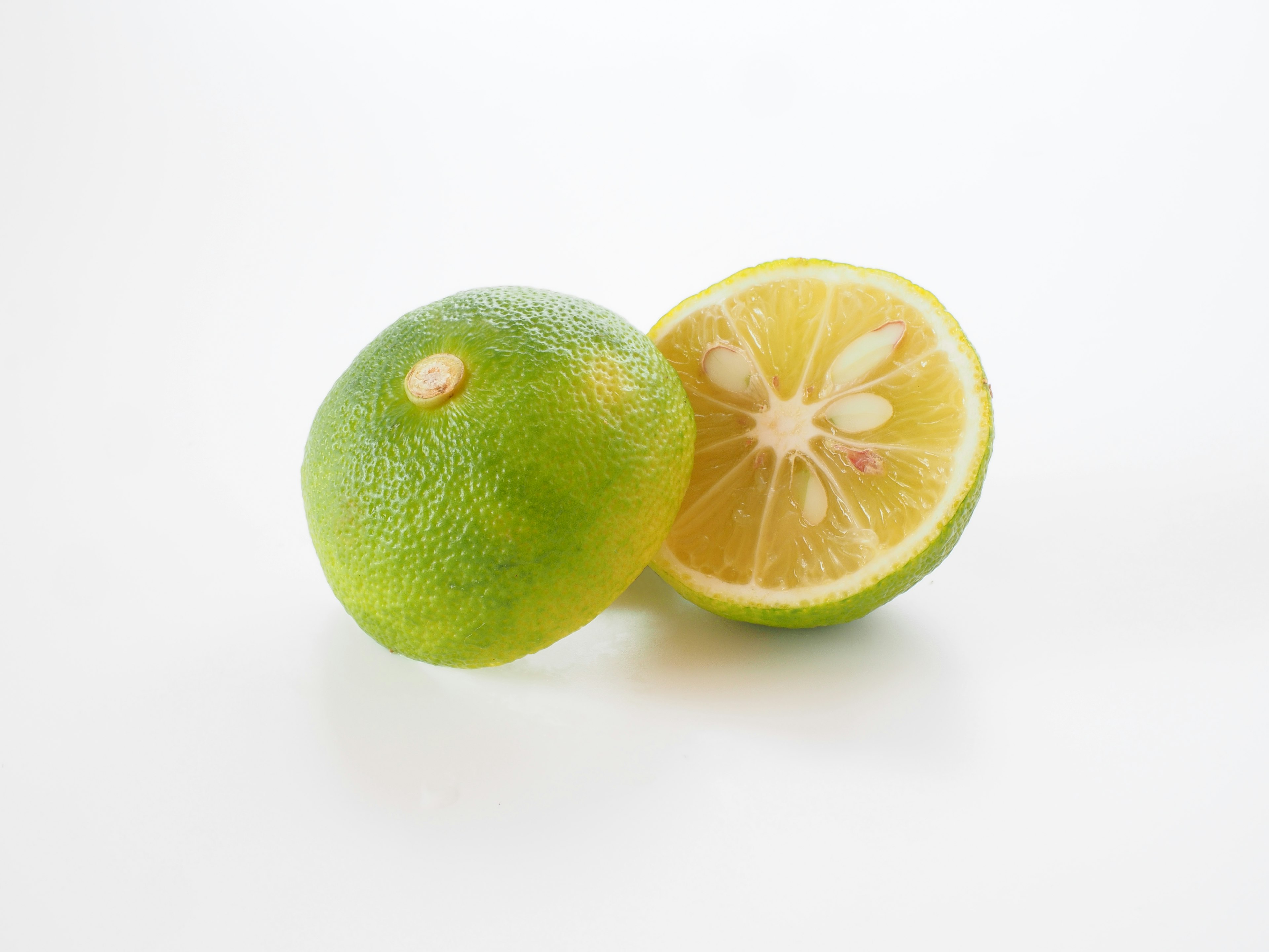 Green lime and a halved lime placed on a white background